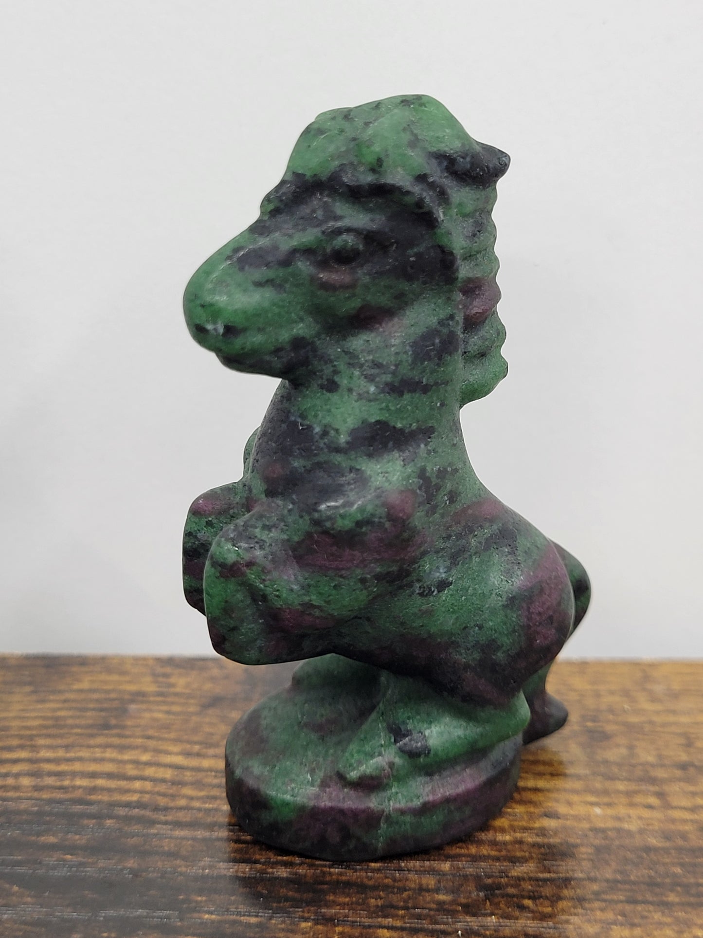 A Ruby Zoisite horse-shaped stone carving displayed on a wooden shelf.