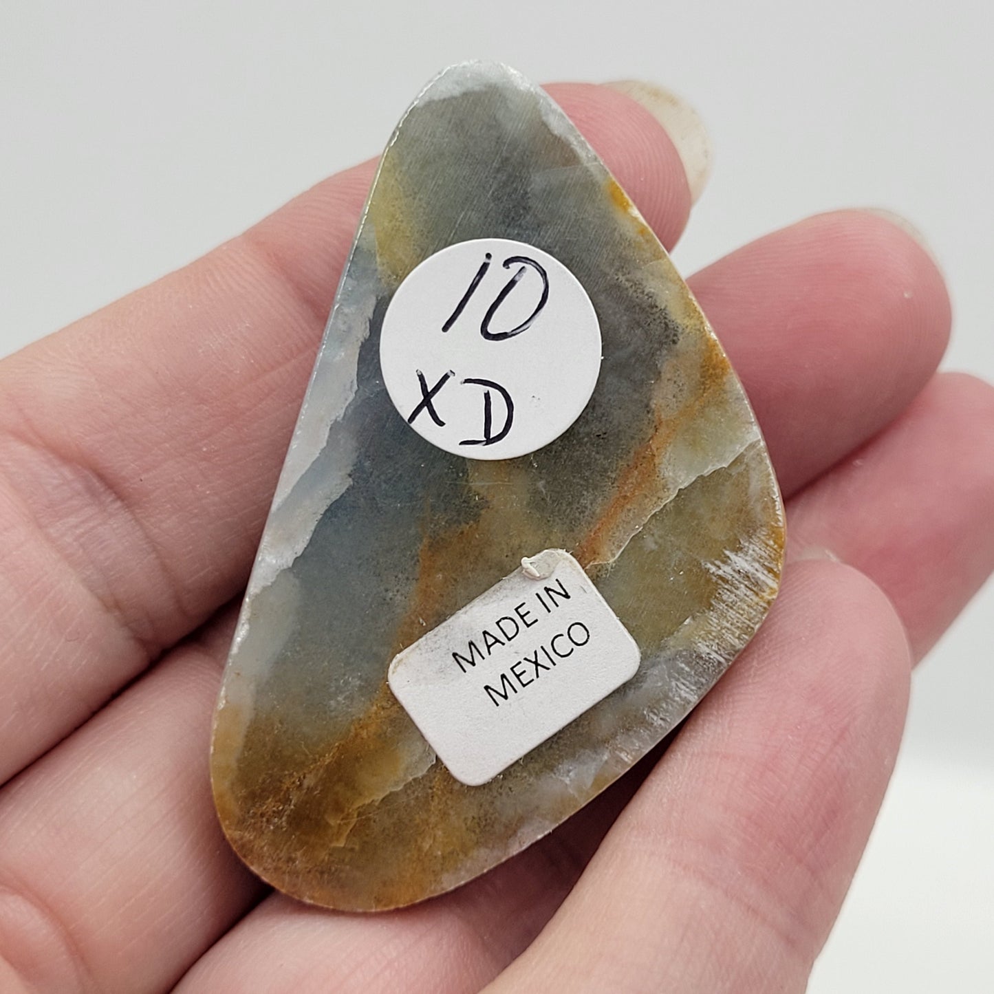 Blue Onyx cabochon with yellow veins held in a hand against a white background
