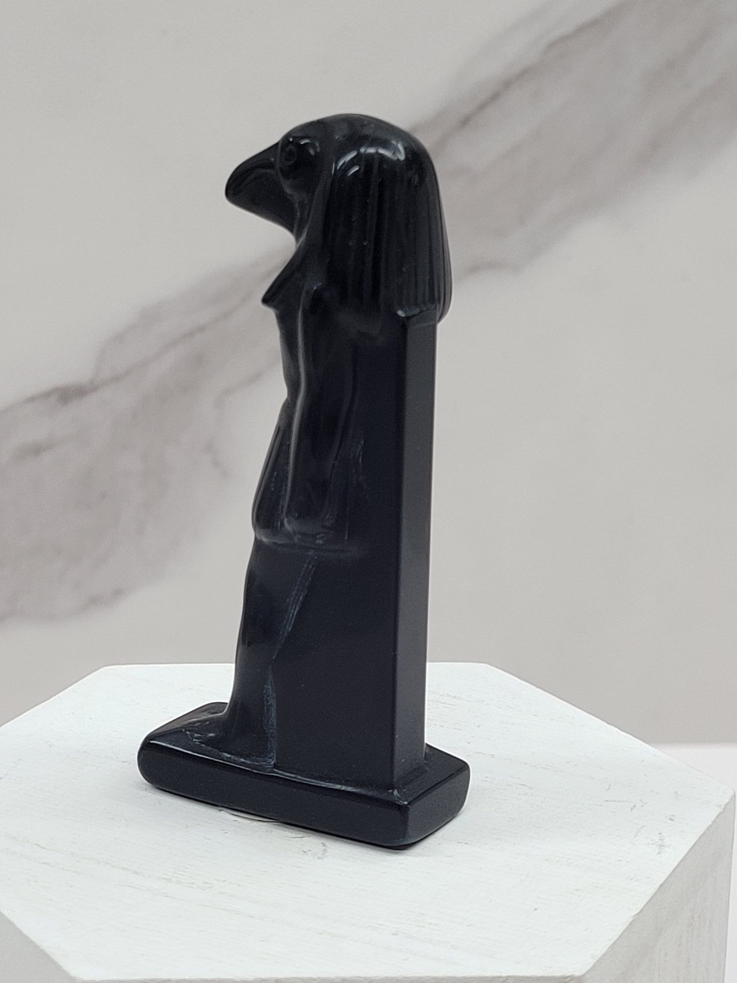 A black obsidian carving of Horus, a falcon-headed deity, on a white base