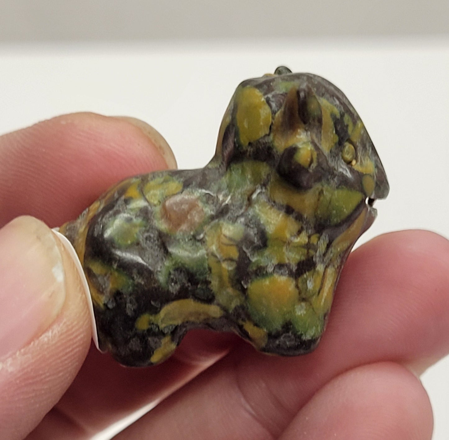Hand holding an Ajooba Jasper highland cow carving on a white background