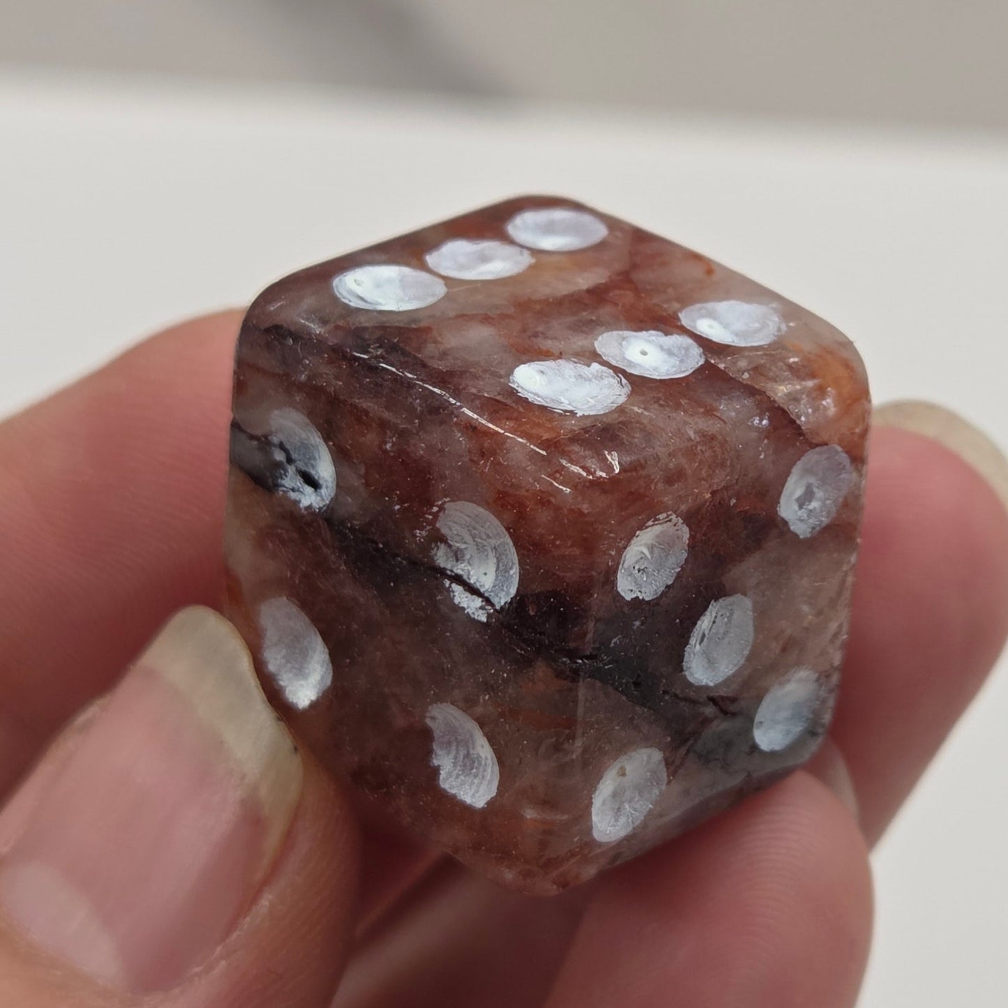 Hand holding a brown die with white dots against a neutral background