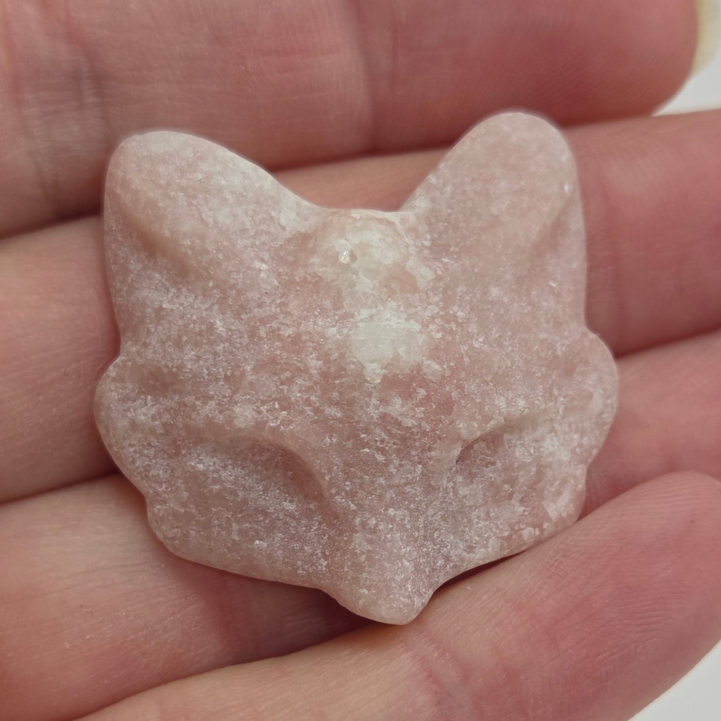 Hand holding a Pink Opal crystal fox mask carving