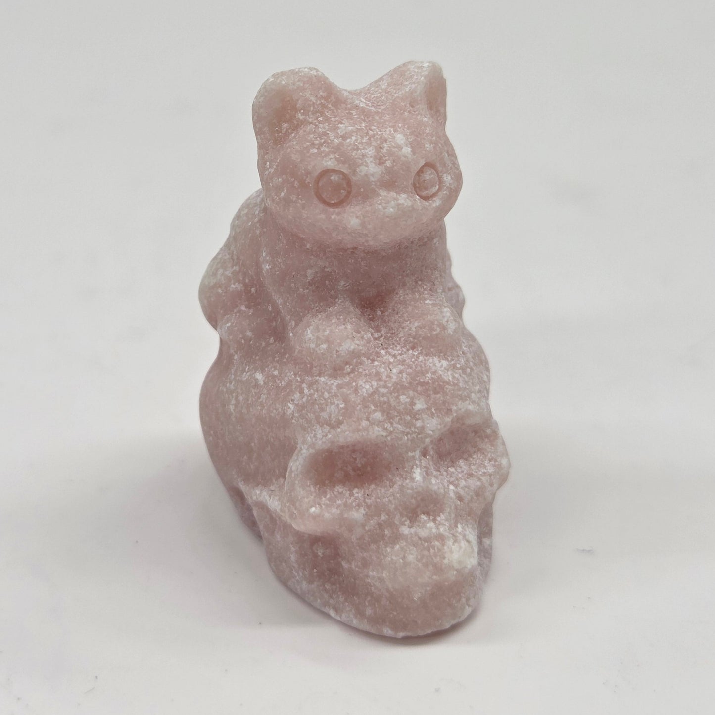 Pink Opal skull carving with a cat sitting on it on a white background