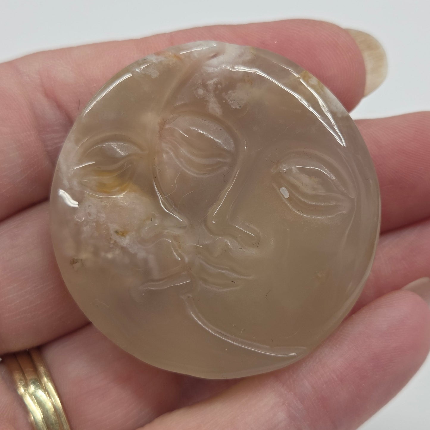 Flower Agate stone with engraved faces resembling a sun and moon on a white background