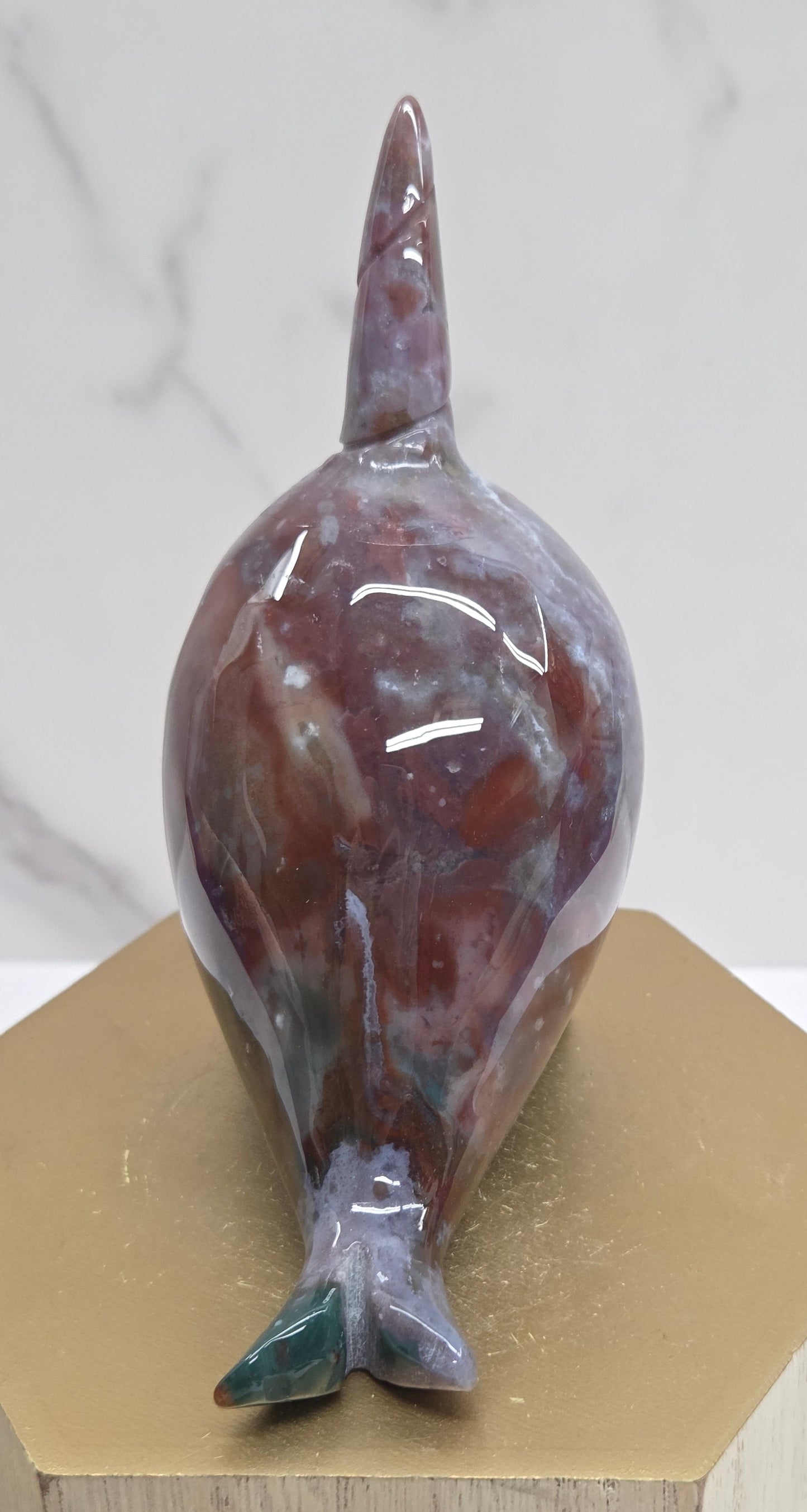 Sea Jasper Narwhal carving, with purple and green coloring, on a wood stand against a white background