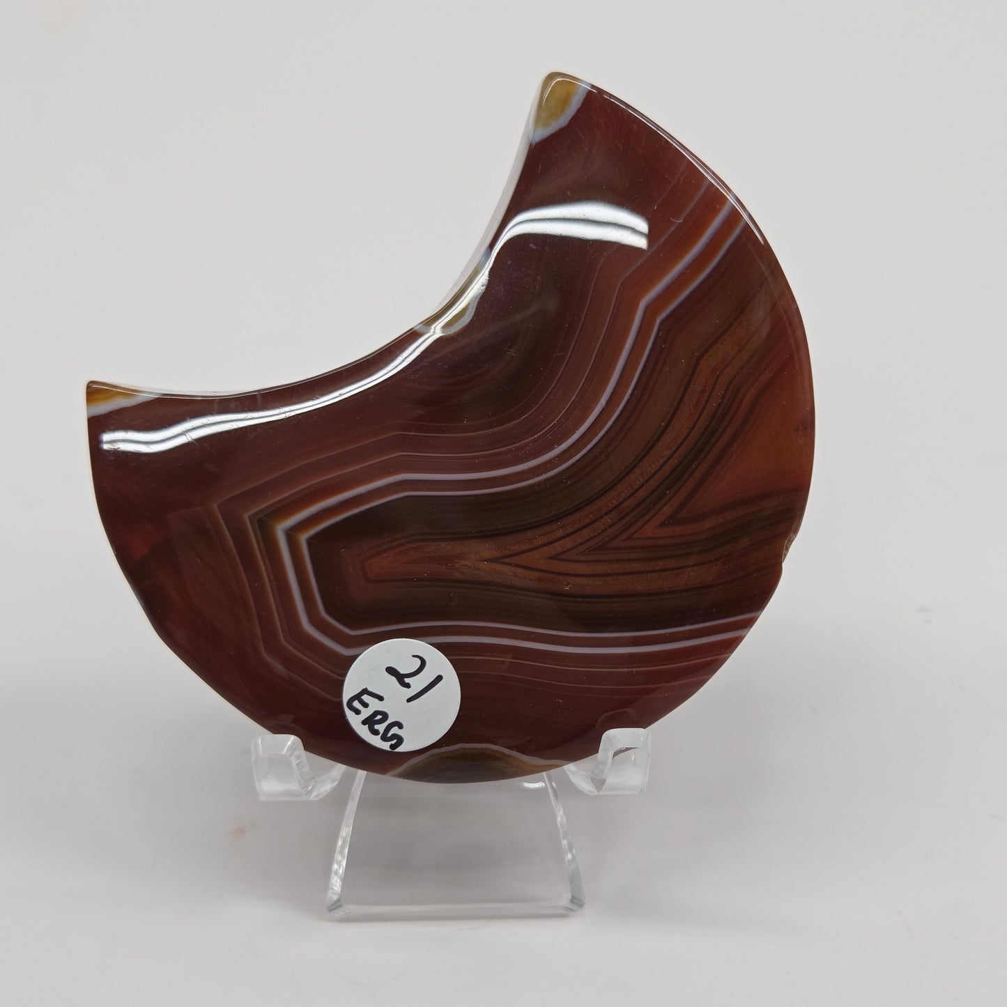 banded Carnelian crescent moon carving on a clear stand against a white background