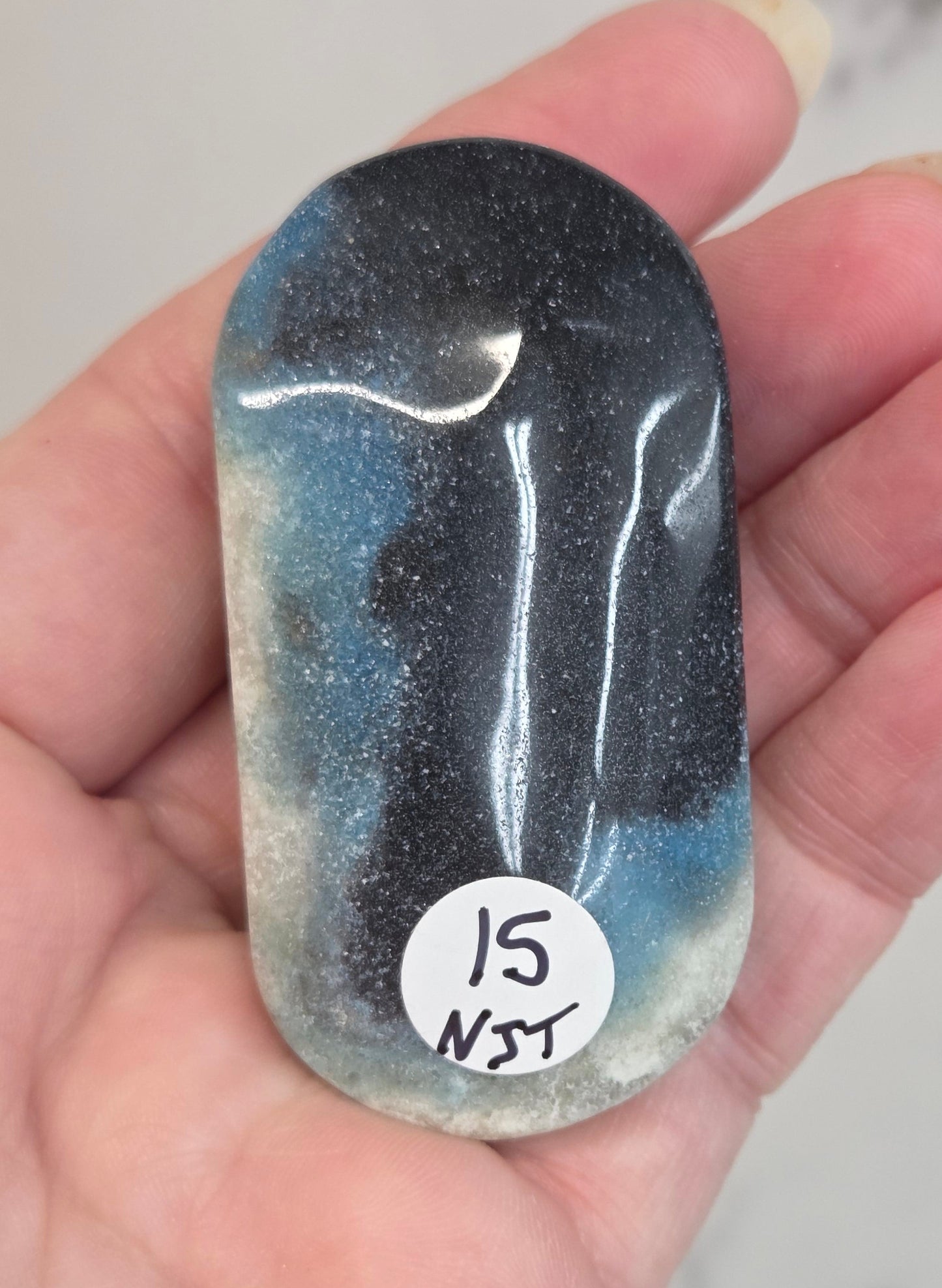 Hand holding a Trolleite polished palm stone on a white background
