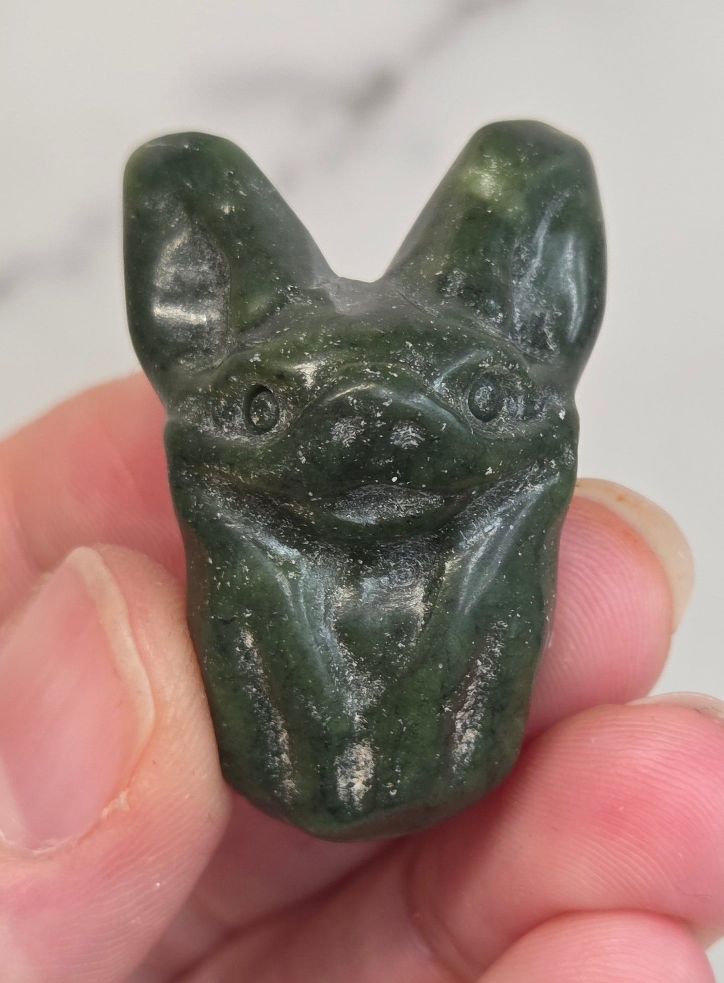 Green Jade bat-shaped carving held between fingers against a white background