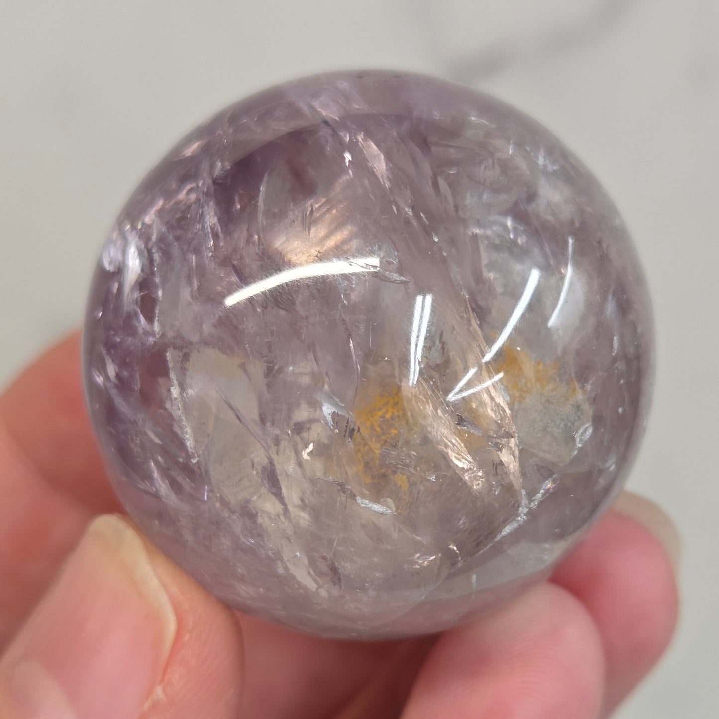 Hand holding a Phantom Amethyst sphere on a white background
