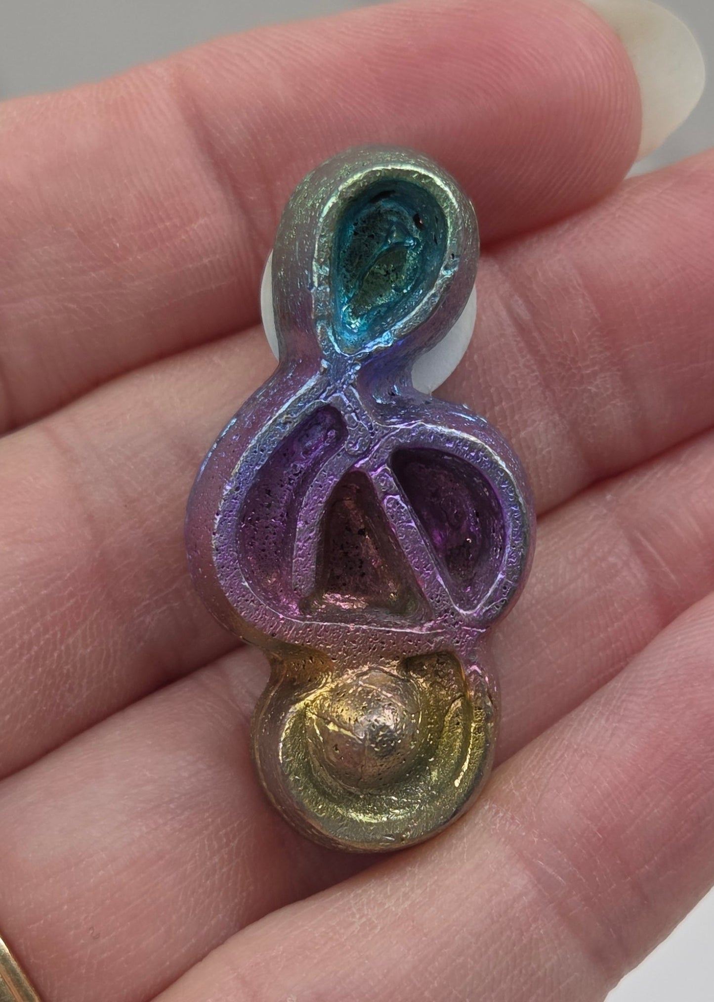 Colorful Bismuth carving shaped like a music symbol held in a hand.