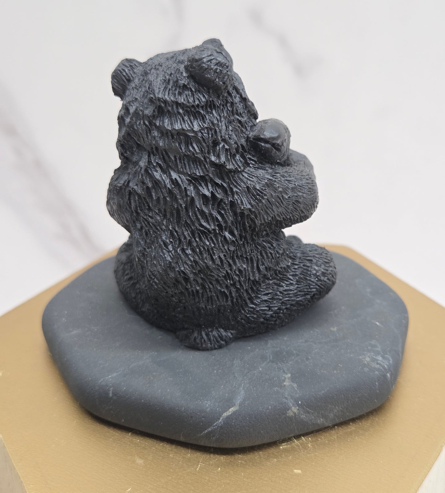 Black bear figurine made of shungite on a gray stone base against a white background