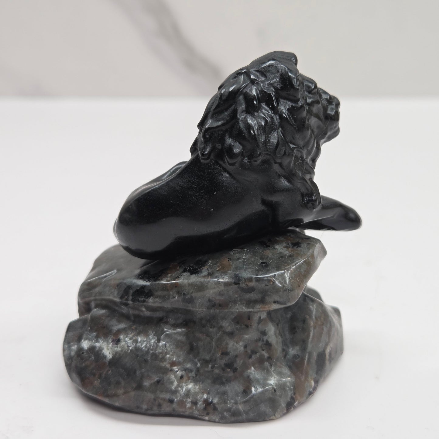 Black Obsidian sculpture of a lion on a grey yooperlite rock on a white background