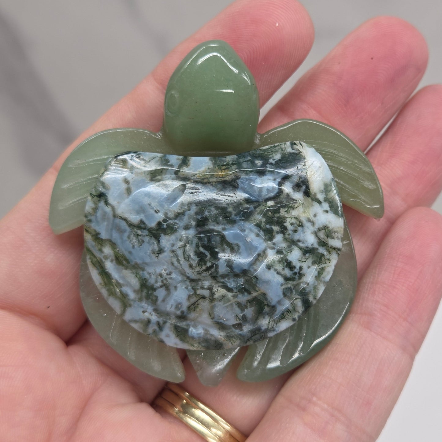 Hand holding a Jade turtle with a Moss Agate shell against a neutral background