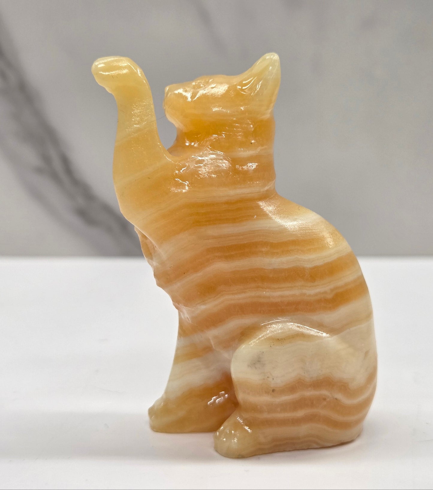 Cat crystal figurine made of Orange Calcite, with banding of orange & white on a white surface with a light gray background