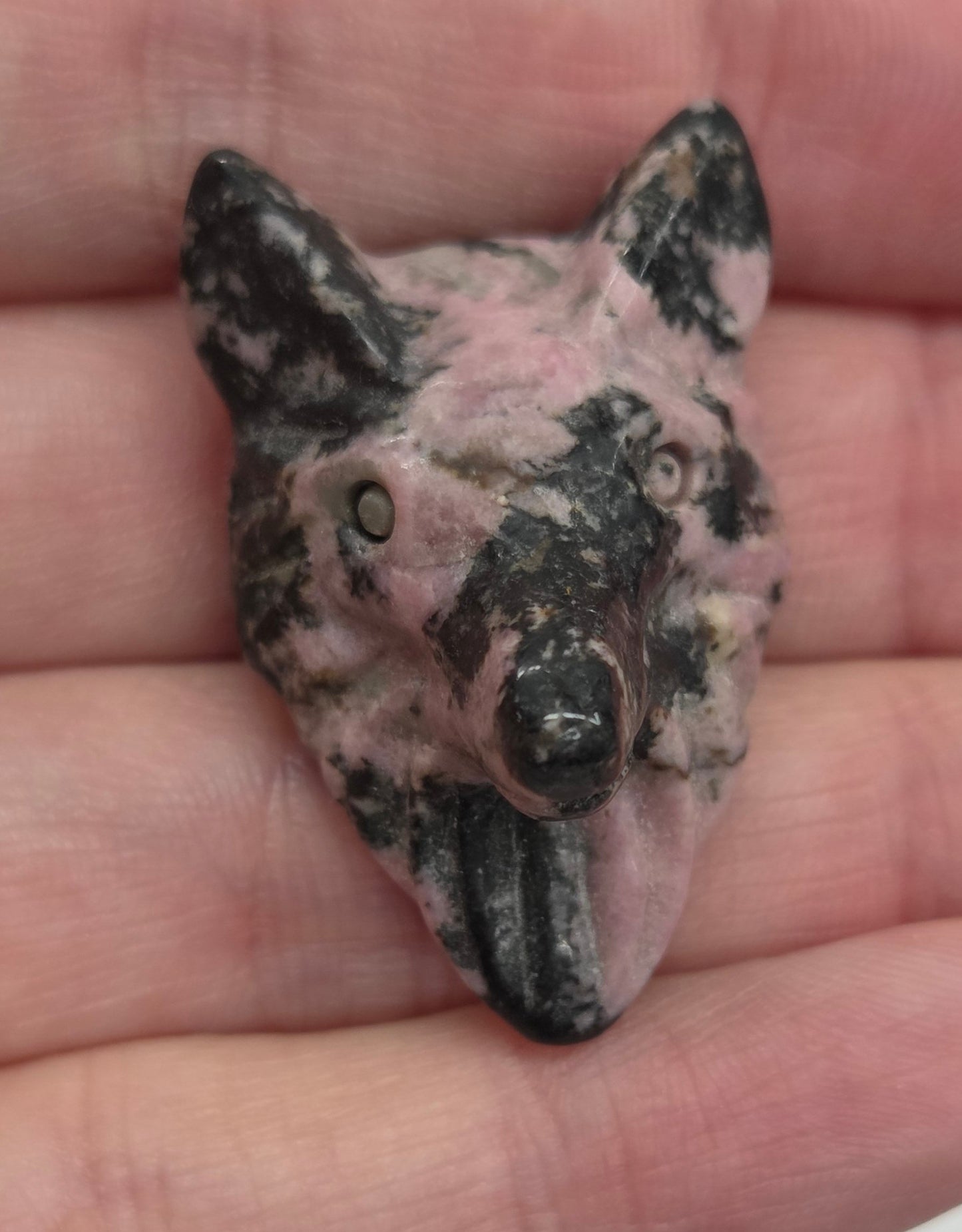Person holding a pink and black Rhodonite carving shaped like a wolf face
