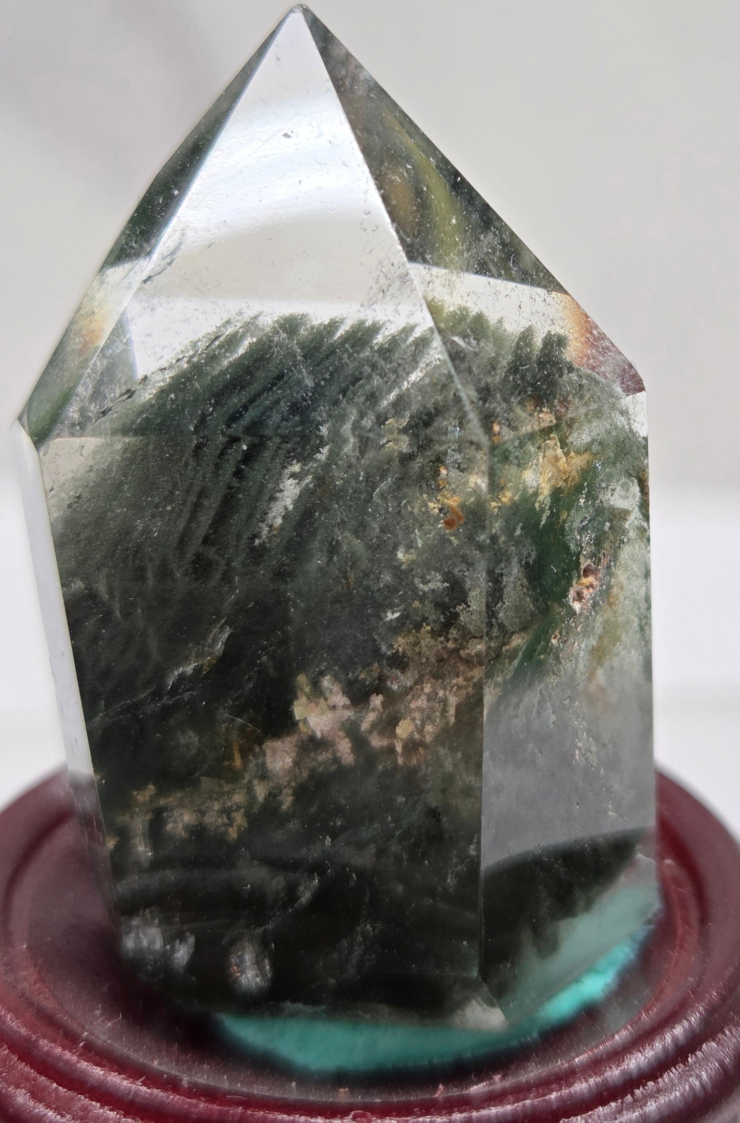 A clear Garden Quartz crystal with inclusions, mounted on a wooden stand with a circular cut-out at the base.