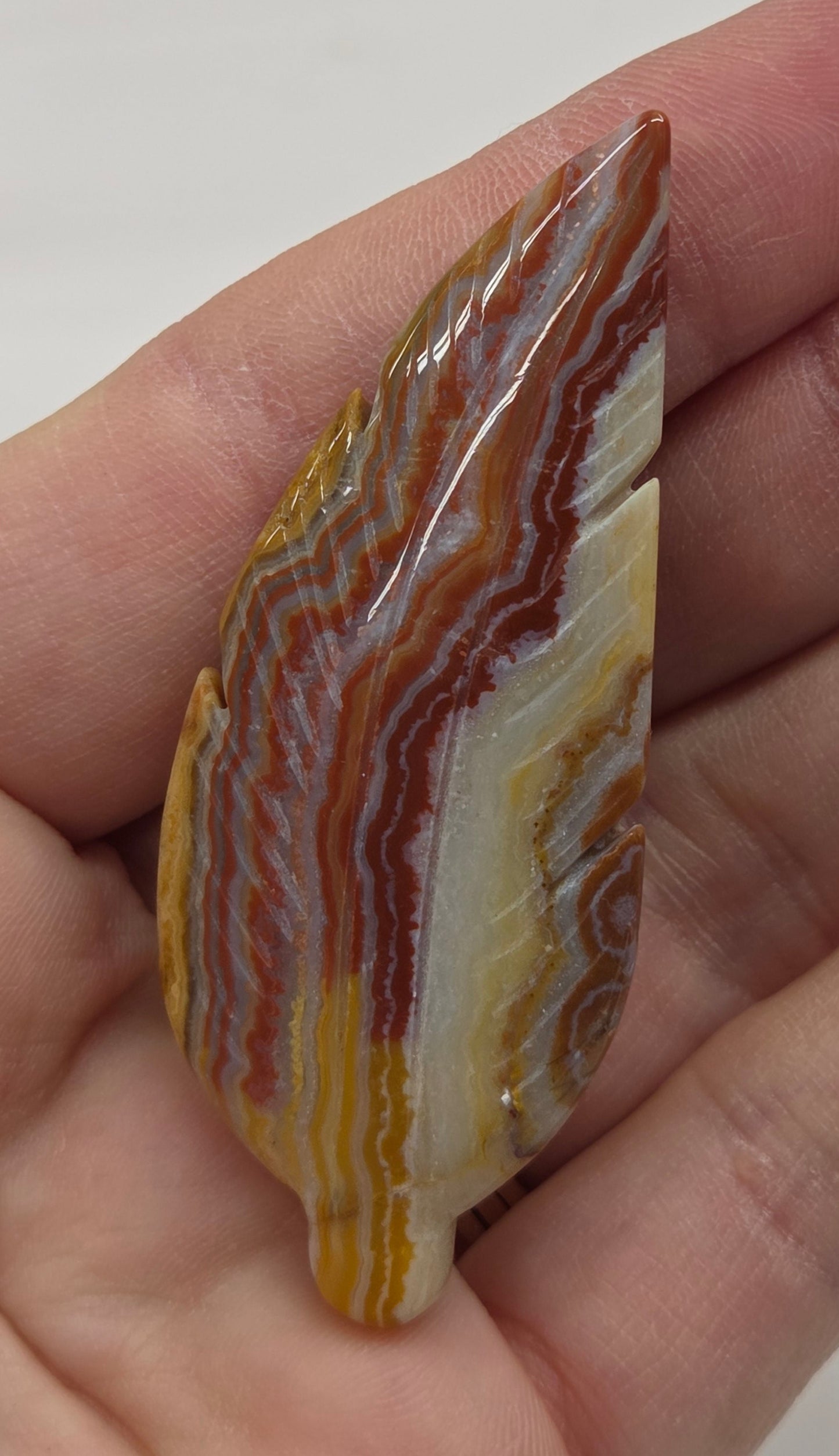 Hand holding a striped jasper feather carving with a plain background