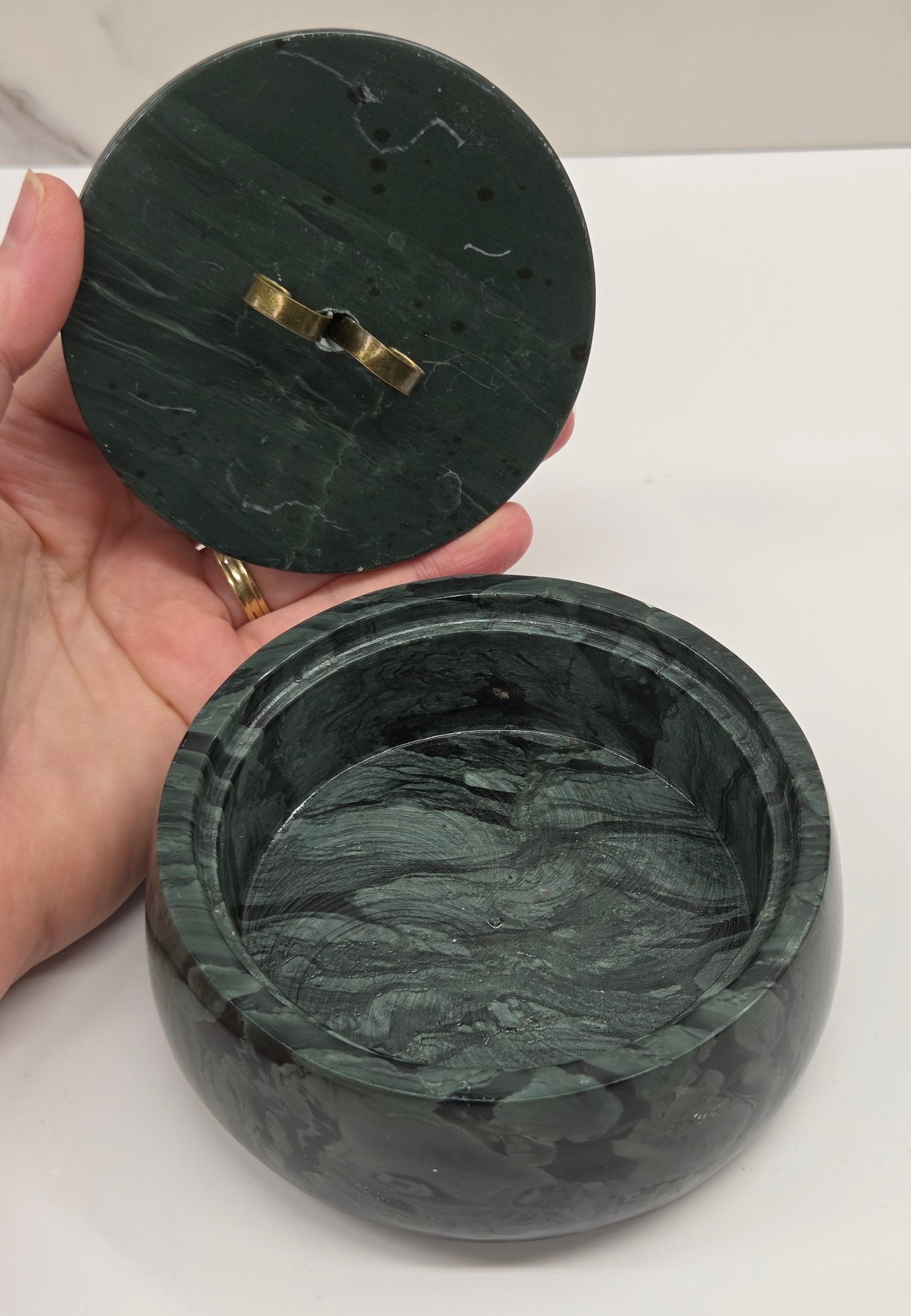 Green wave picture jasper bowl held by a hand on a white surface
