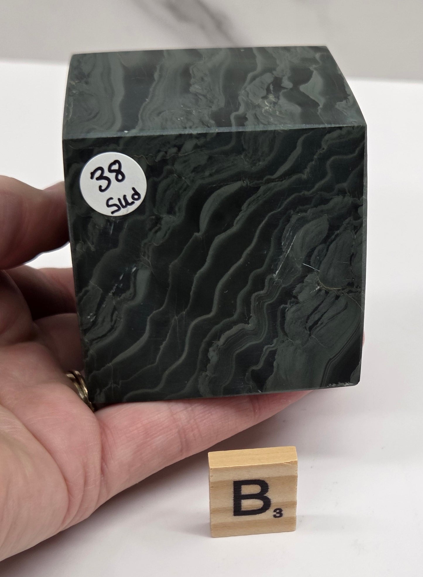 Hand holding a green wave picture jasper cube with a wave like pattern, on a white background
