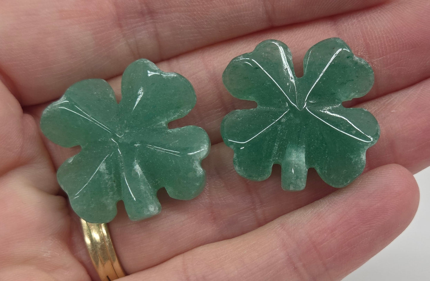 Set of green aventurine 4 leaf clover carvings being held in a hand on a white background