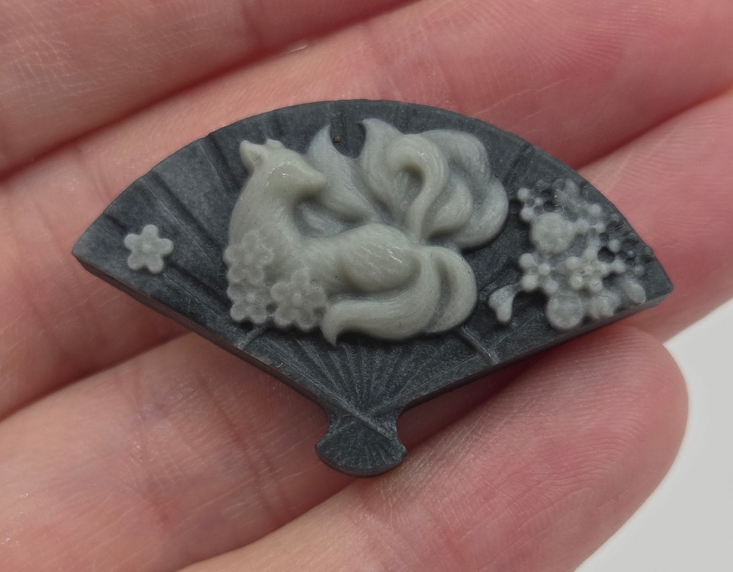 Hand holding a Tai Chi fan carving with a design of a 9 tail fox