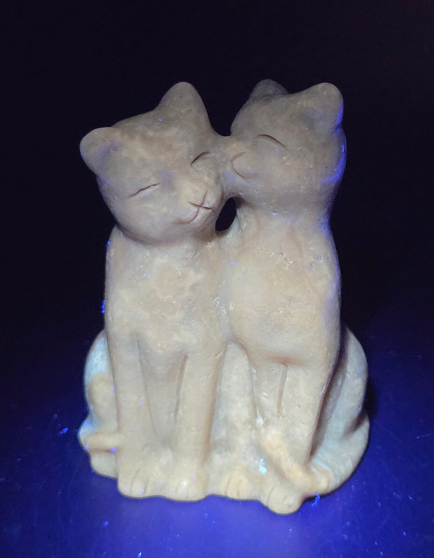 Brown amber calcite carving of a cat couple on a white background under UV light