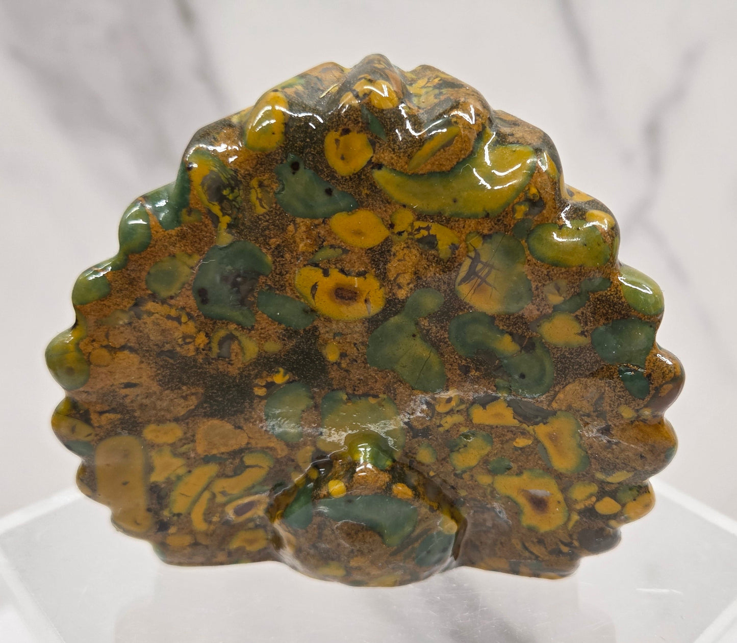 Decorative ajooba jasper peacock carving on a clear stand against a white background