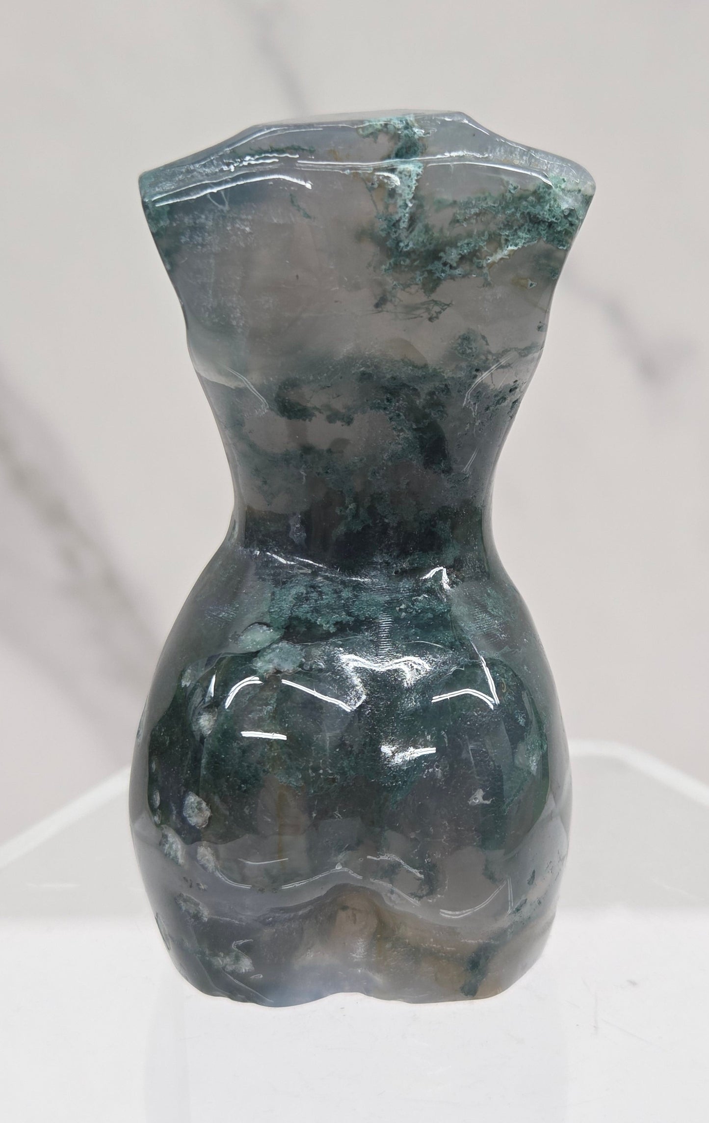 Moss agate carving of abstract human figures on a white surface with a marble-patterned wall in the background.