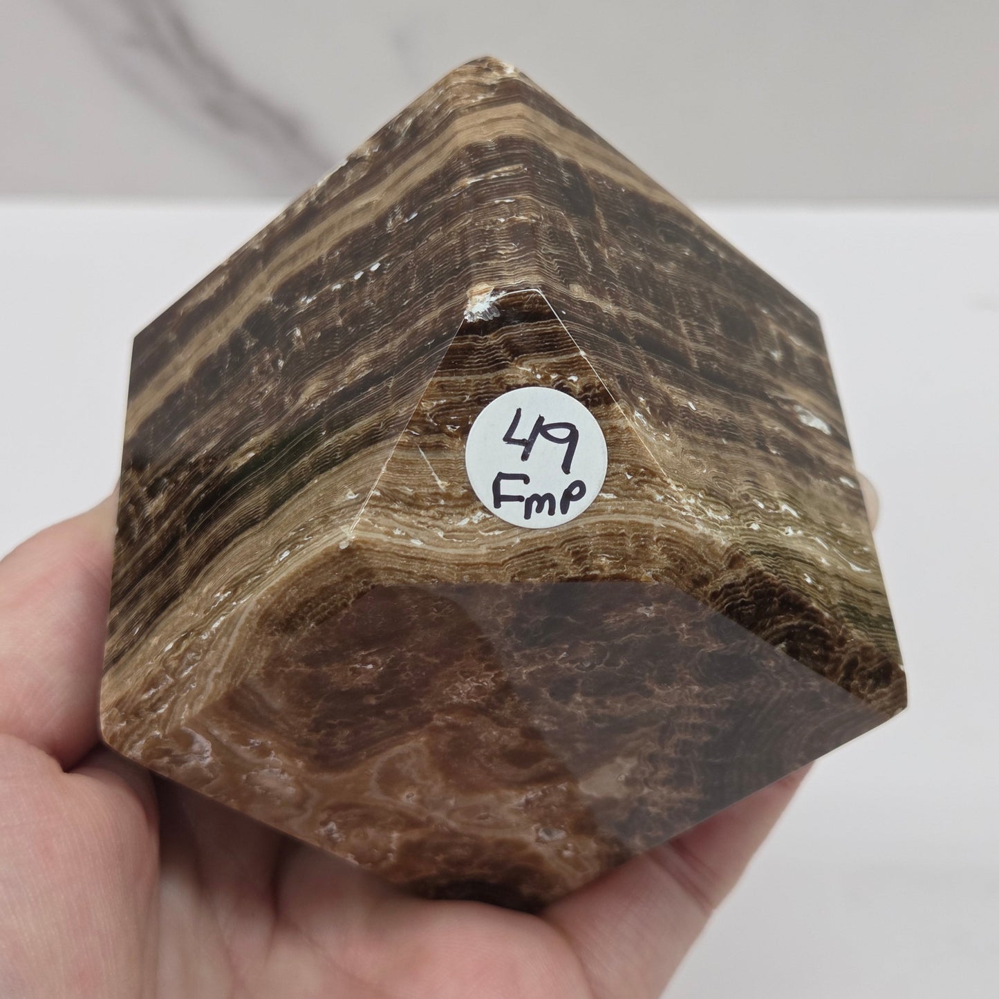 Hand holding a marbled chocolate calcite cube on a white background
