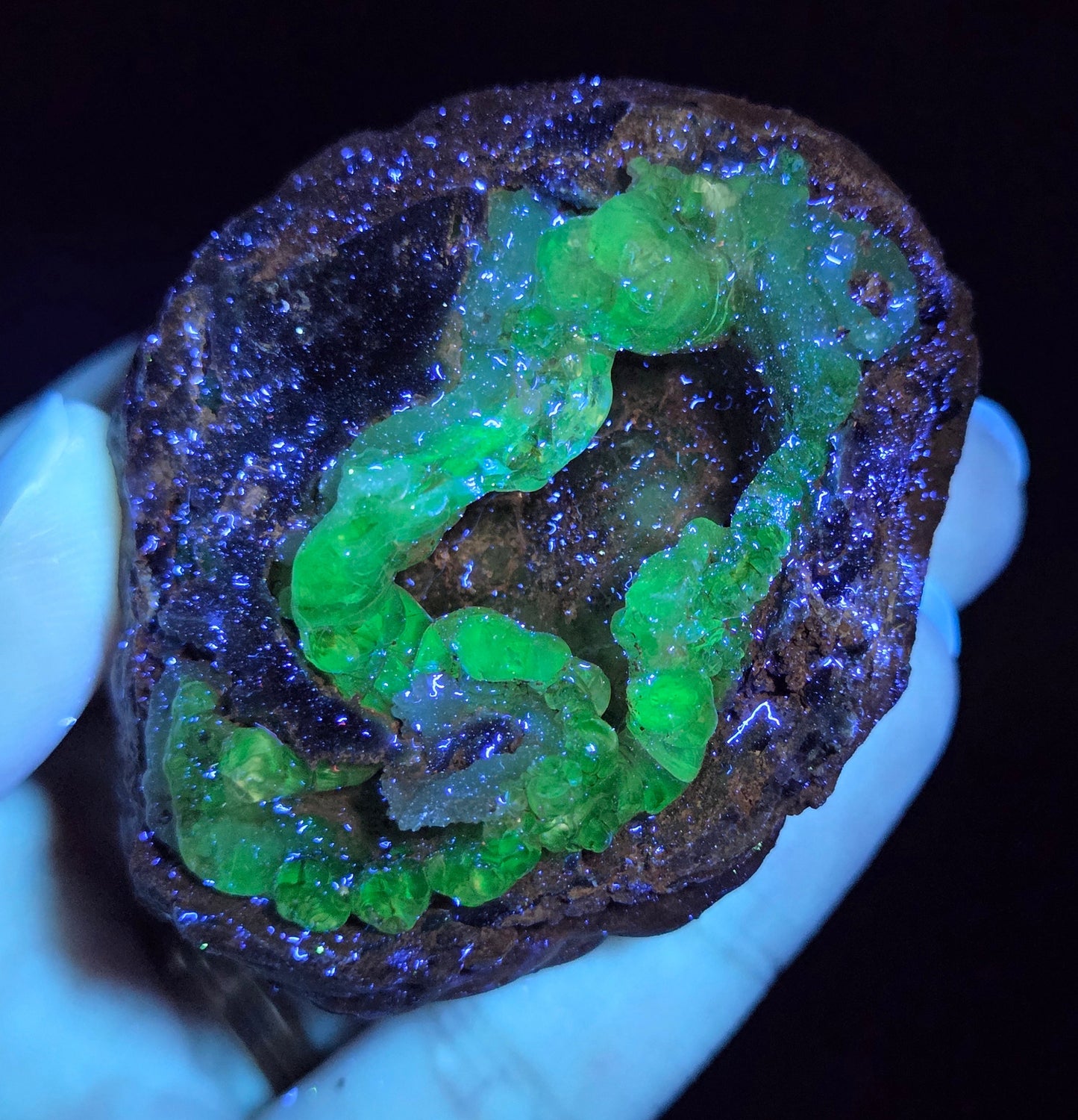 Mineral sample with green fluorescence held by a hand against a dark background