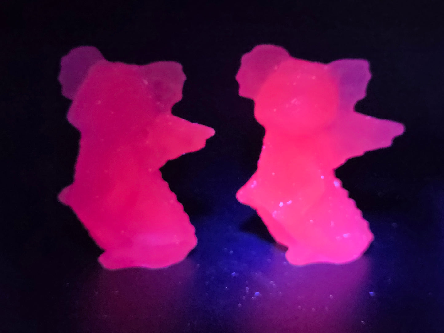 Two pink calcite carvings of dragons under a UV light on a dark surface