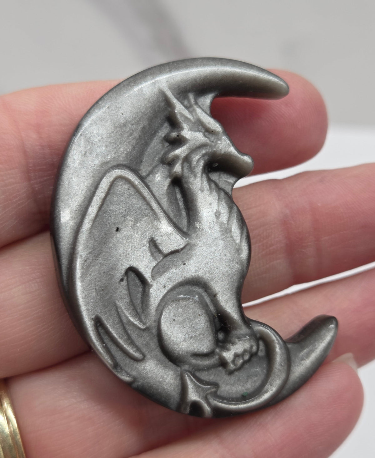 hand holding a silver sheen obsidian dragon-shaped carving on a white background