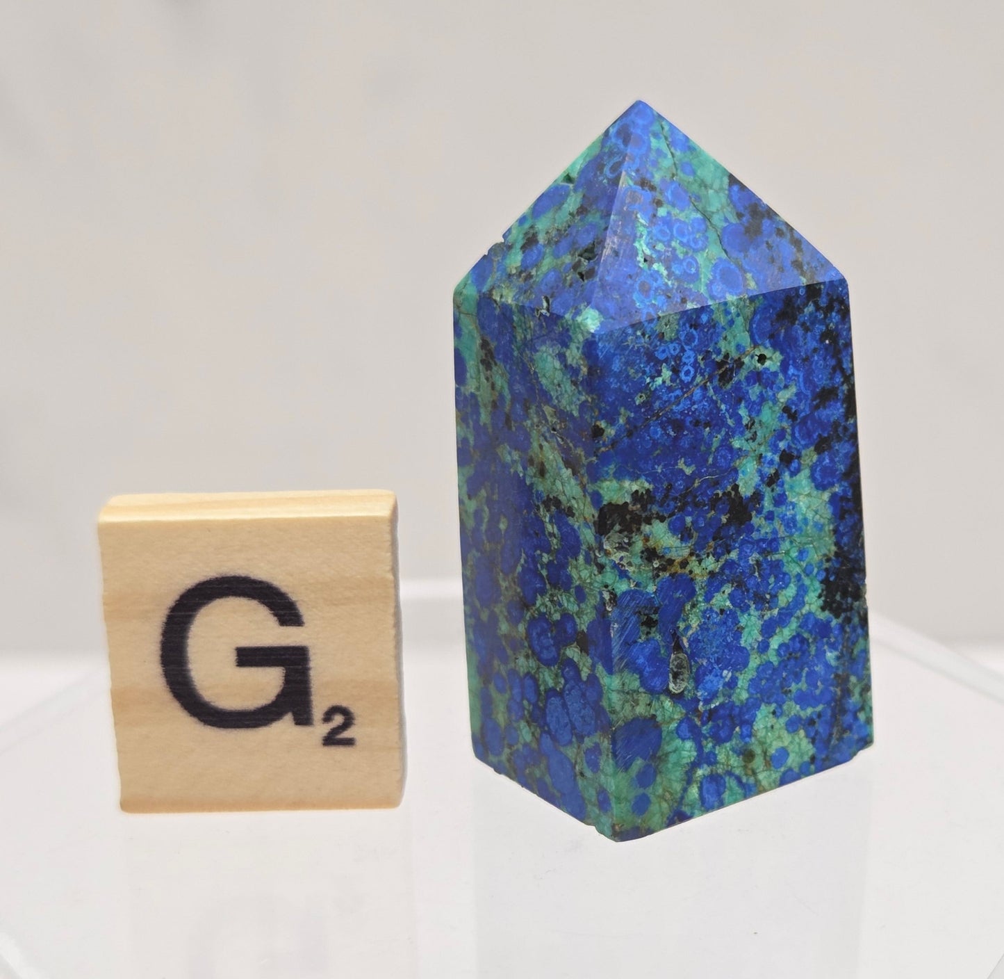 Blue-green Azurite & Chrysocolla crystal point on a white surface with a gray background