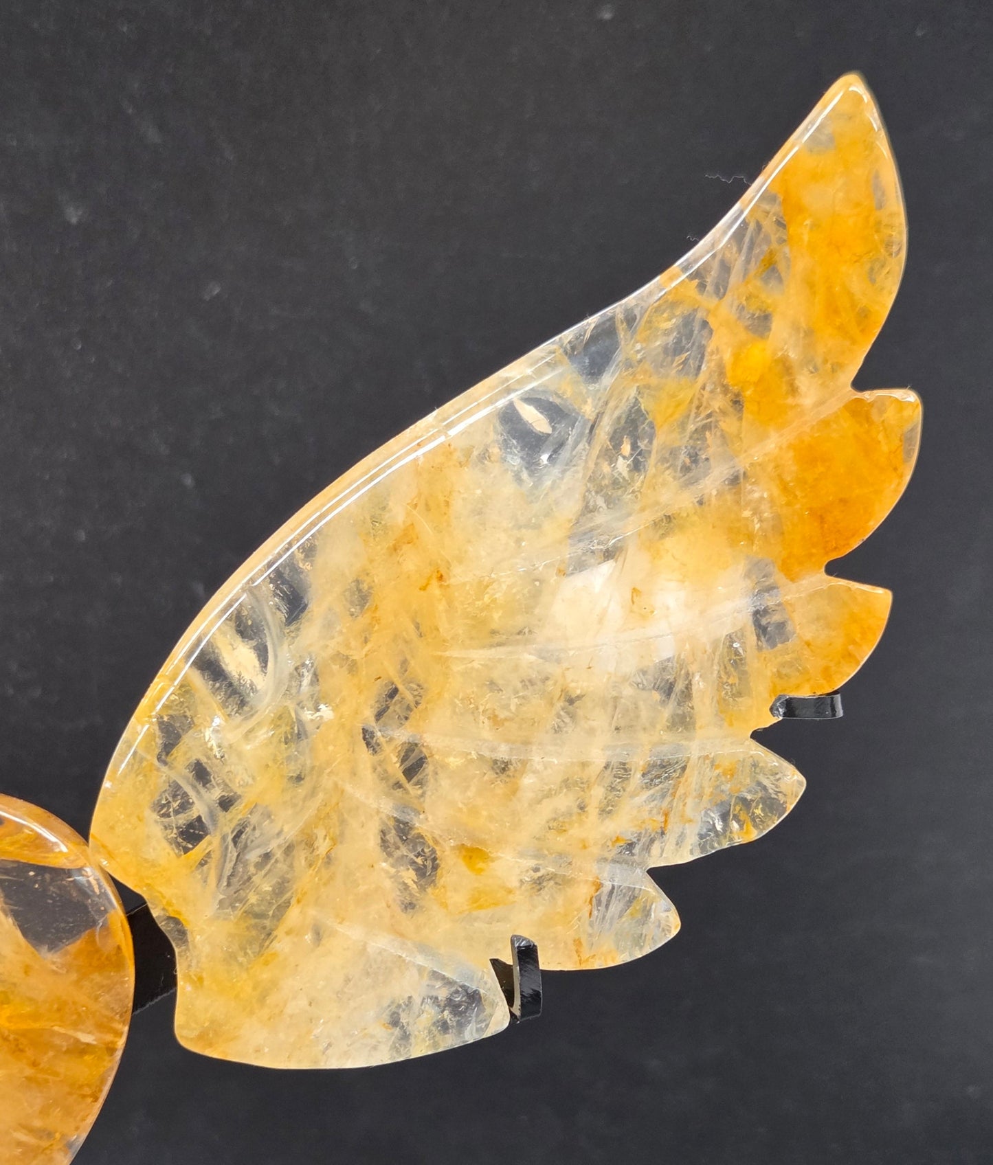 Decorative golden healer wings with a heart on a black stand against a gray background