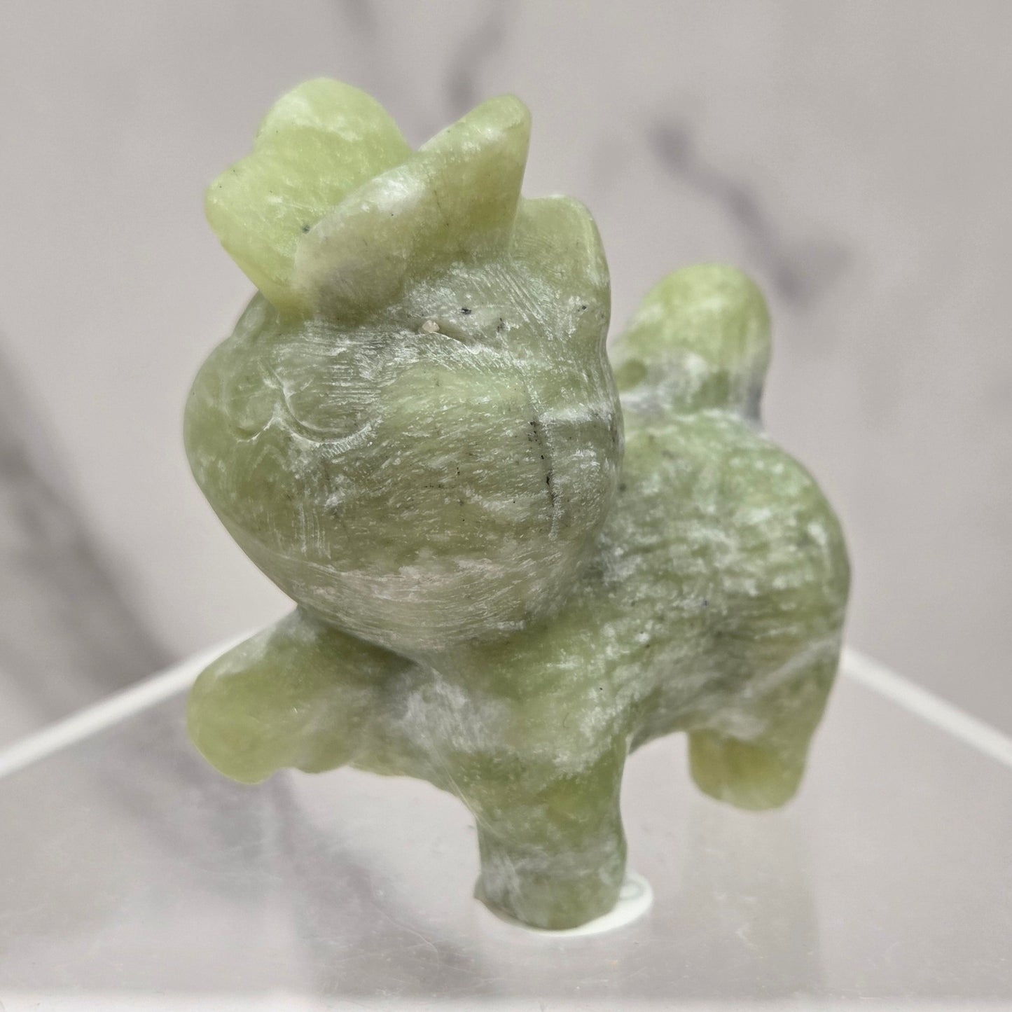 Green stone cat figurine with a butterfly on it's nose on a white surface