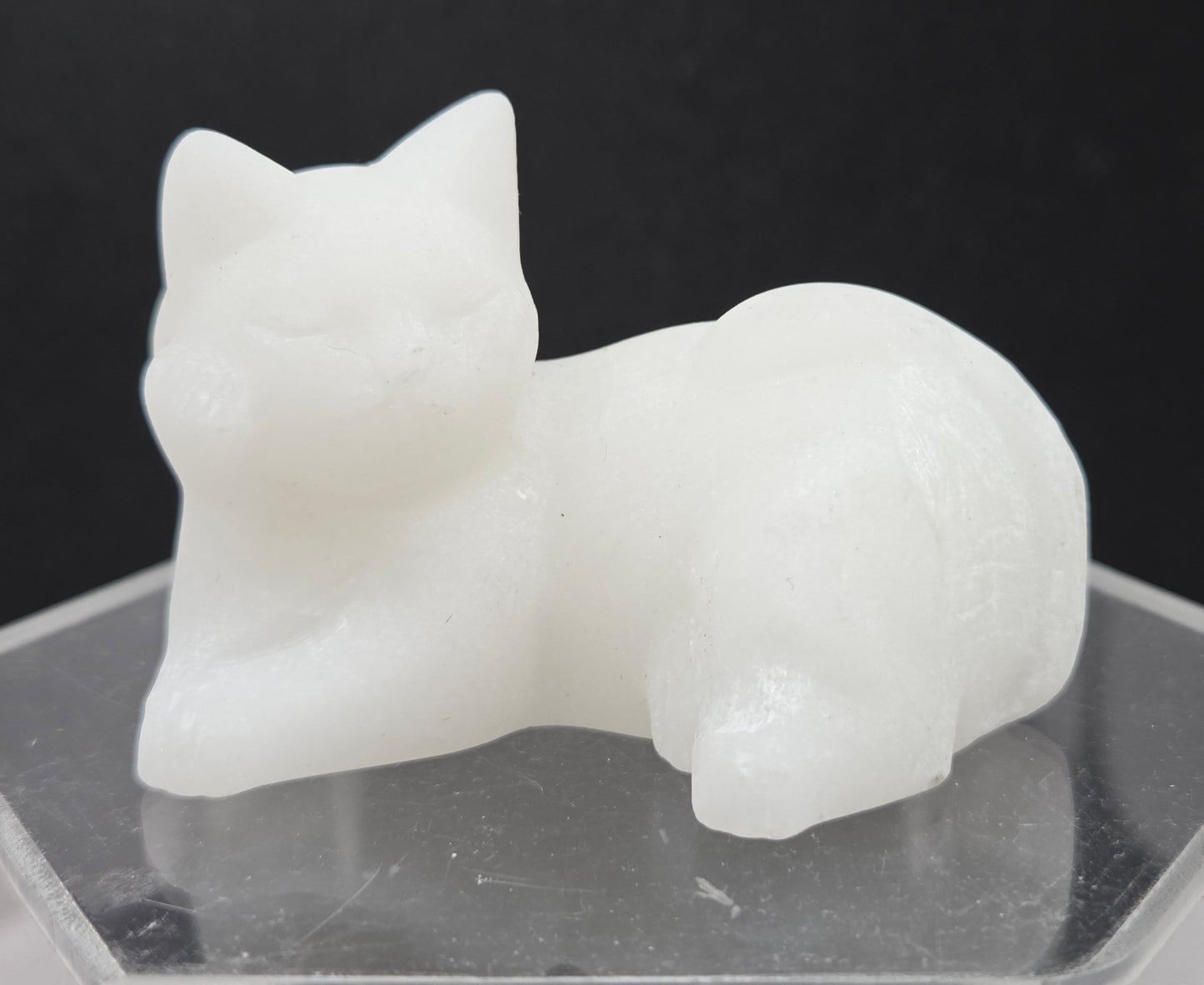 White Jade cat carving lying down an acrylic stand against a neutral background