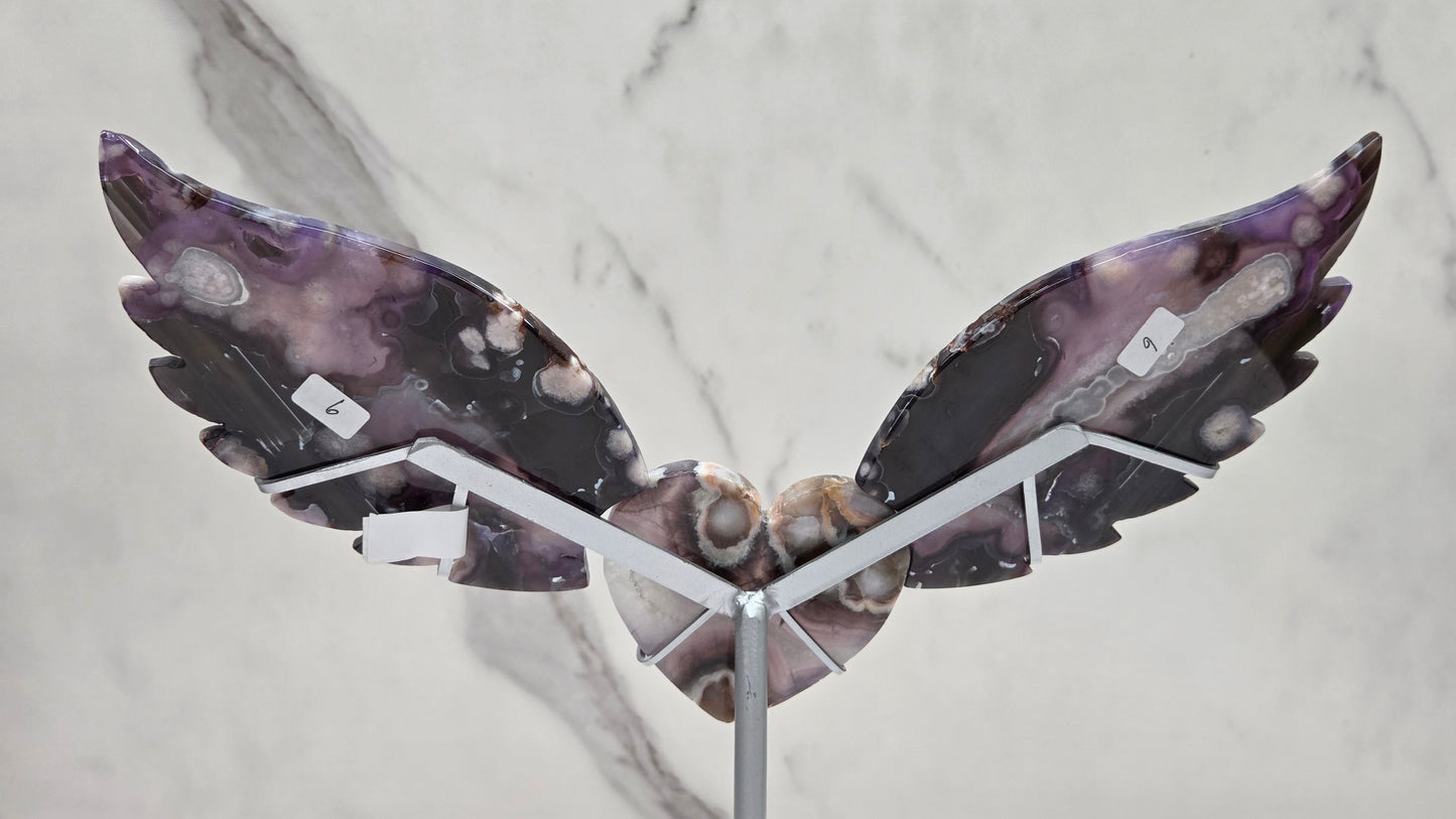 Black Flower Agate carved into wings and hearts on a silver stand against a white background.