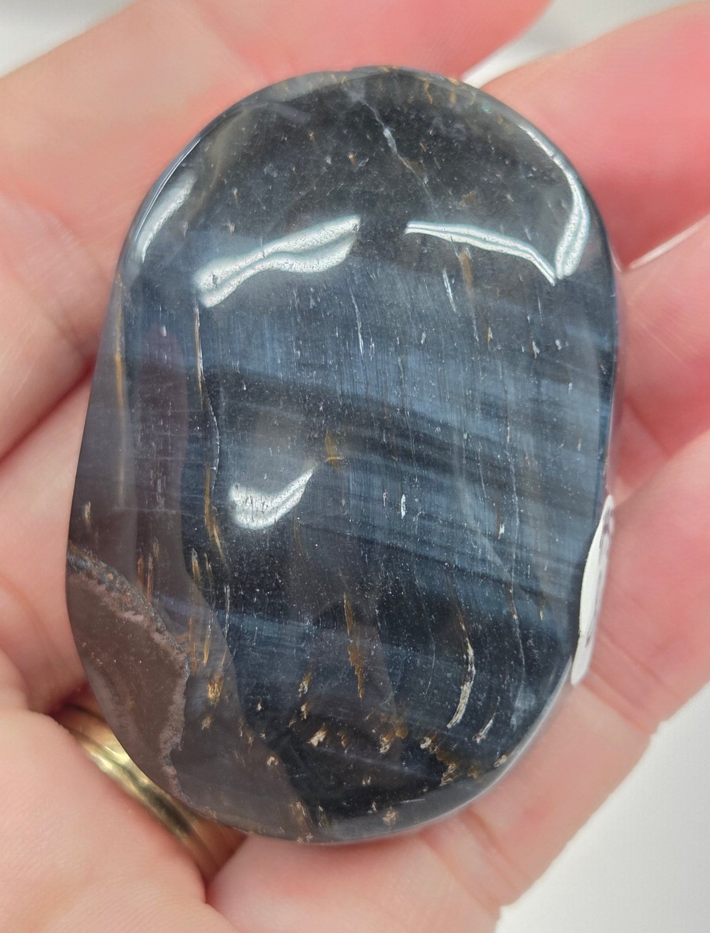Blue Tiger's Eye palm carving being held in a hand against a white background