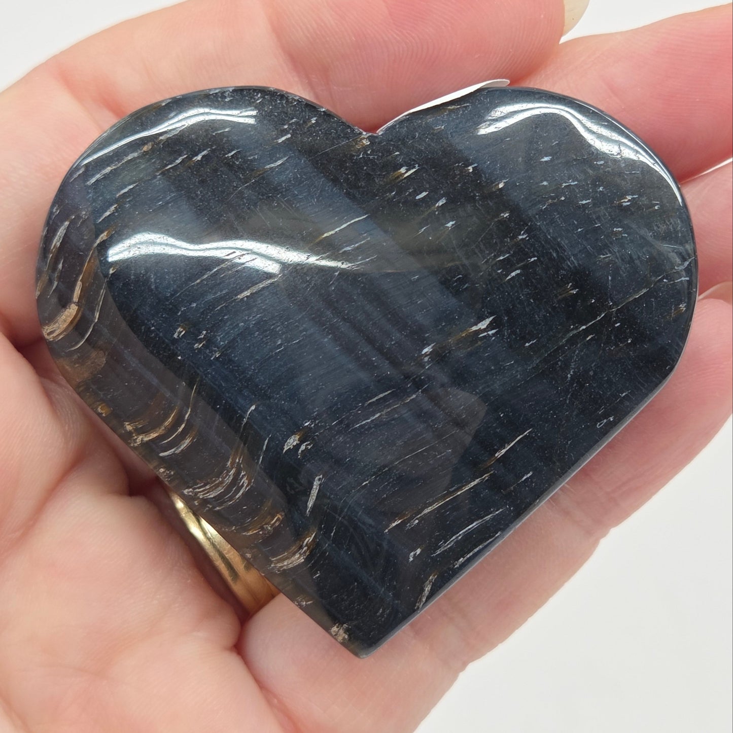 Blue Tiger's Eye heart carving being held in a hand against a white background