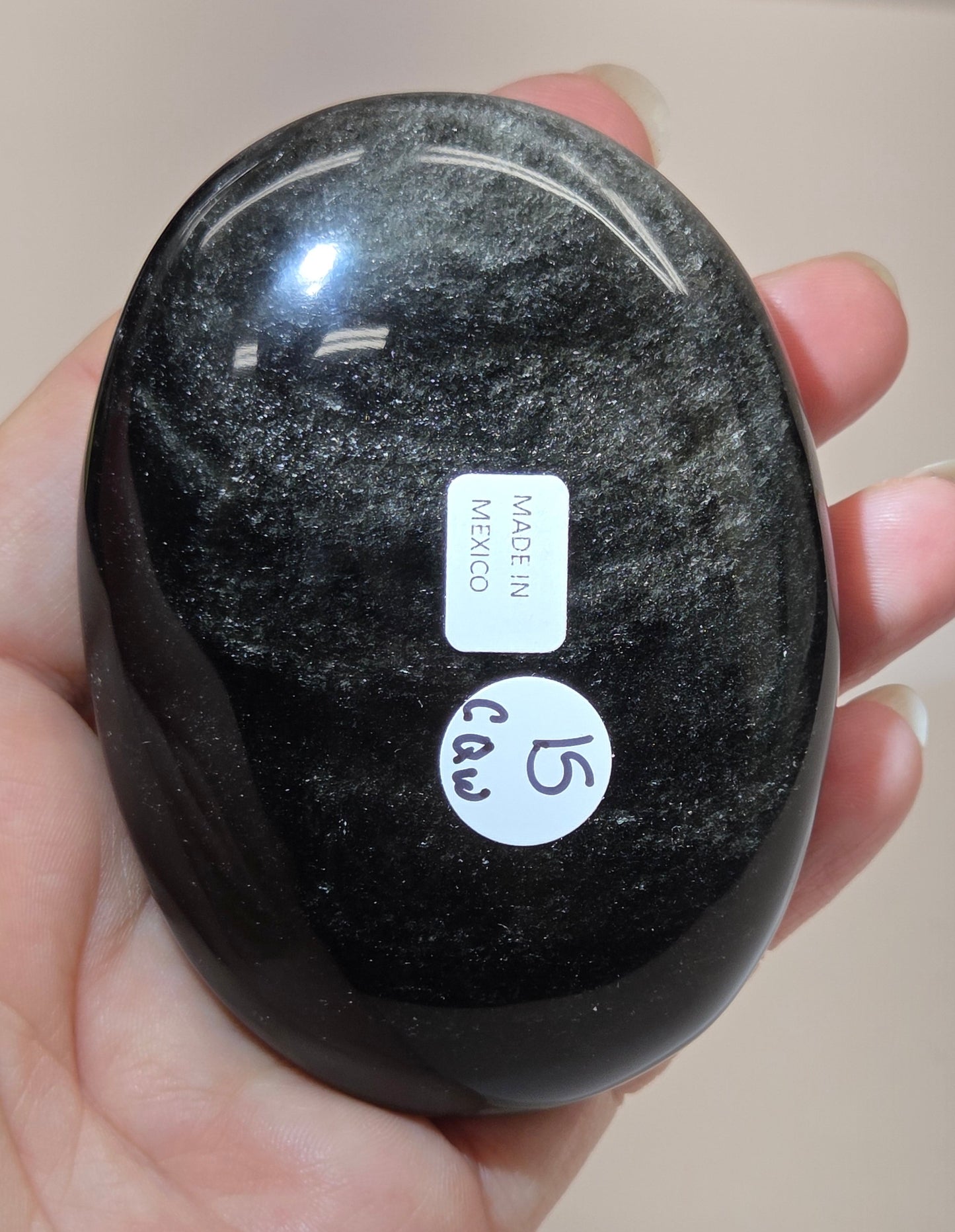 Silver sheen obsidian palm carving being held in a hand against a white background