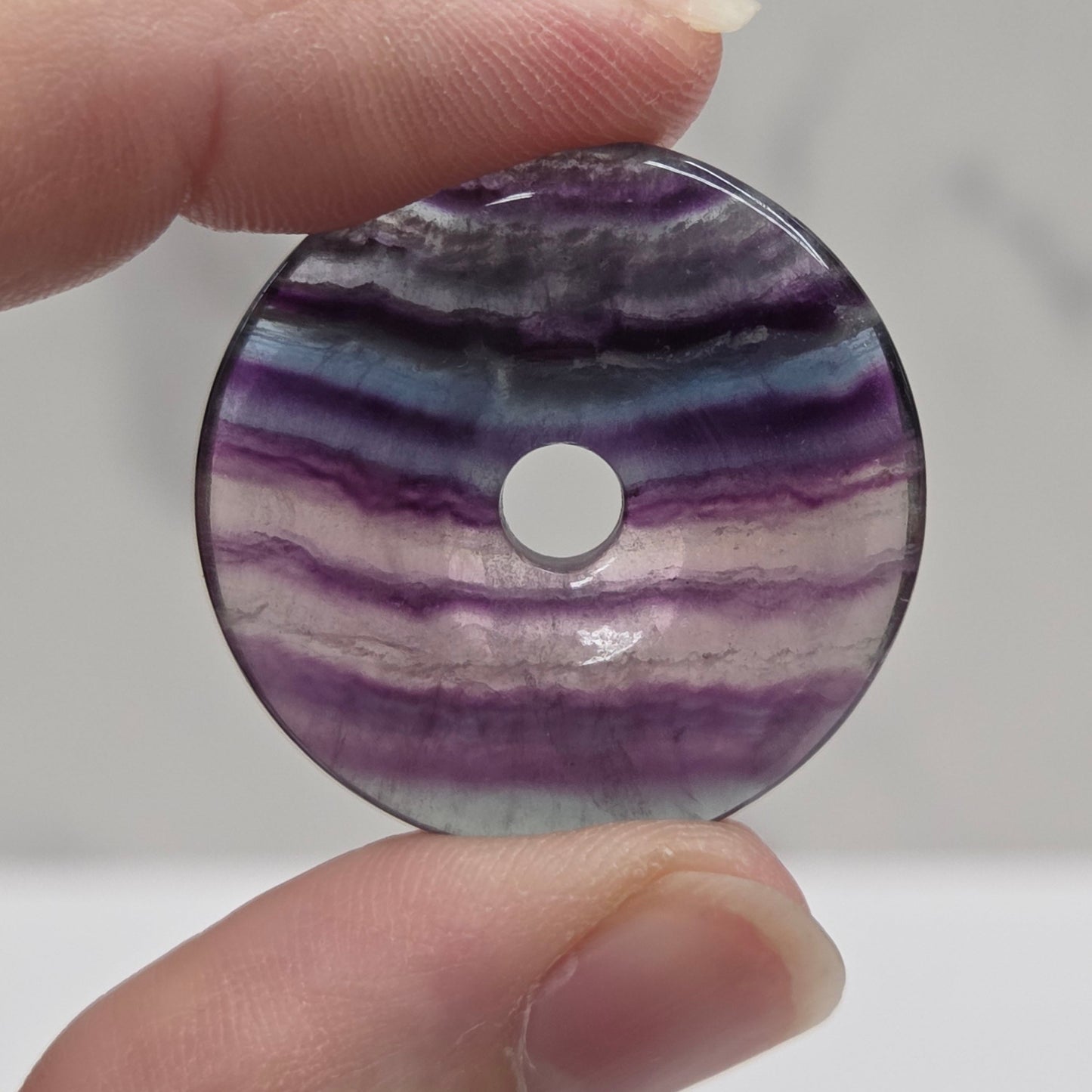 Hand holding a Multi-colored fluorite donut shaped carving with banding on a white background