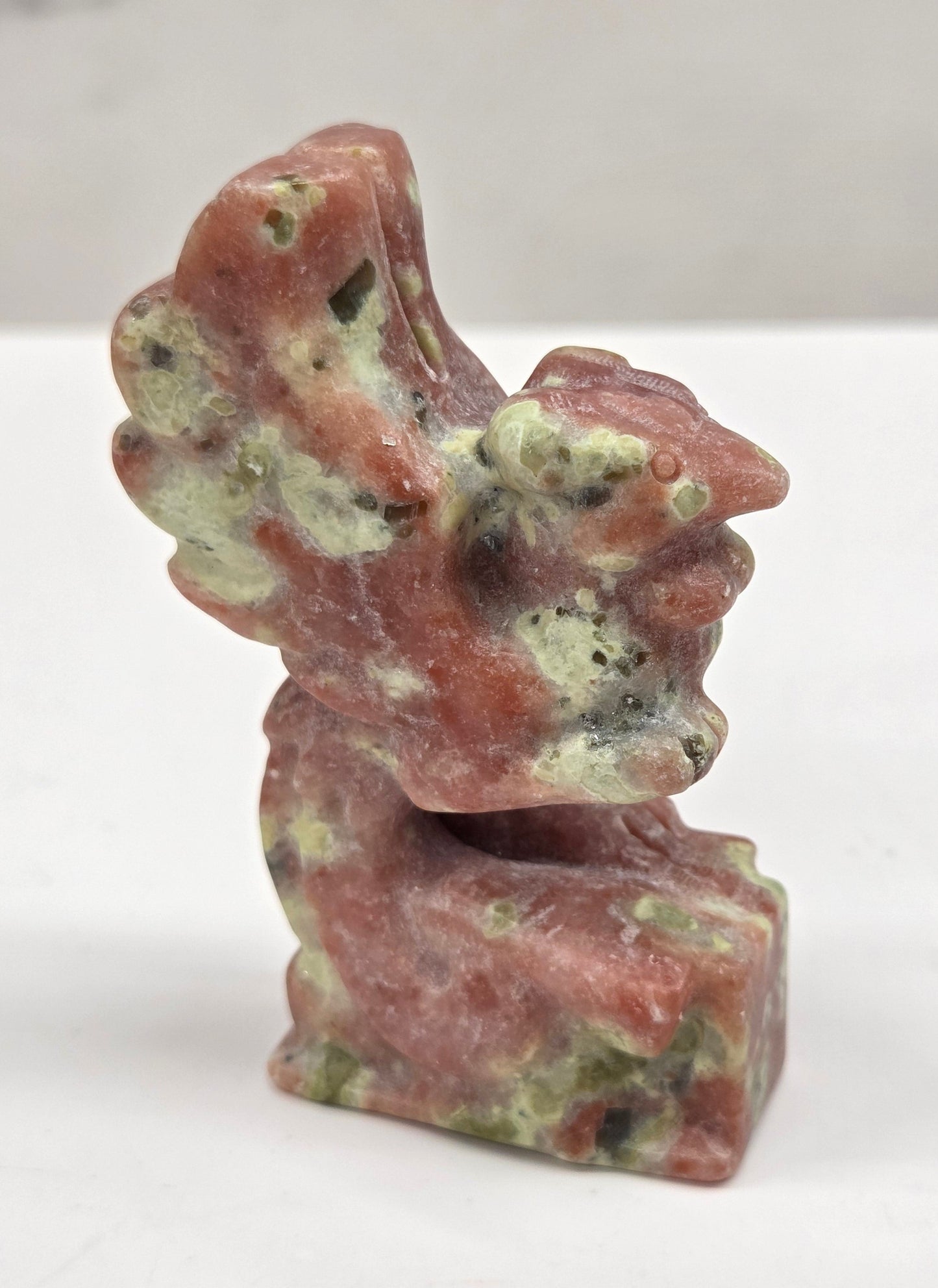Polished red serpentine stone phoenix carving with a natural pattern on a white background