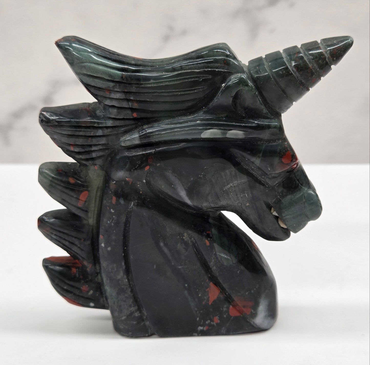 Decorative unicorn carving made of African Bloodstone with black and red design on a white marble background