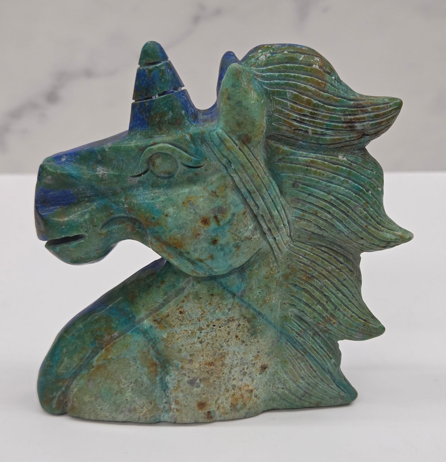 Carved stone unicorn figurine with blue and green patterns on a white background