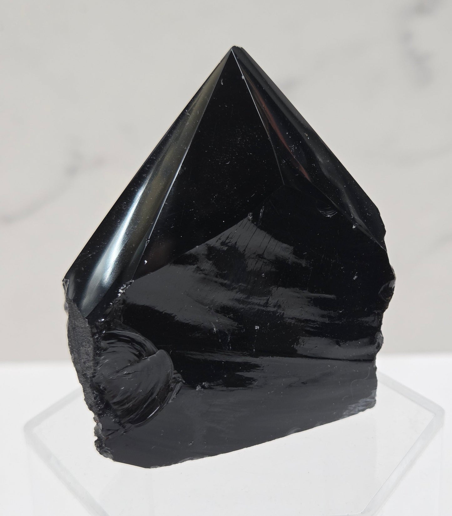 black Obsidian half polished point on a white surface with a gray marble background