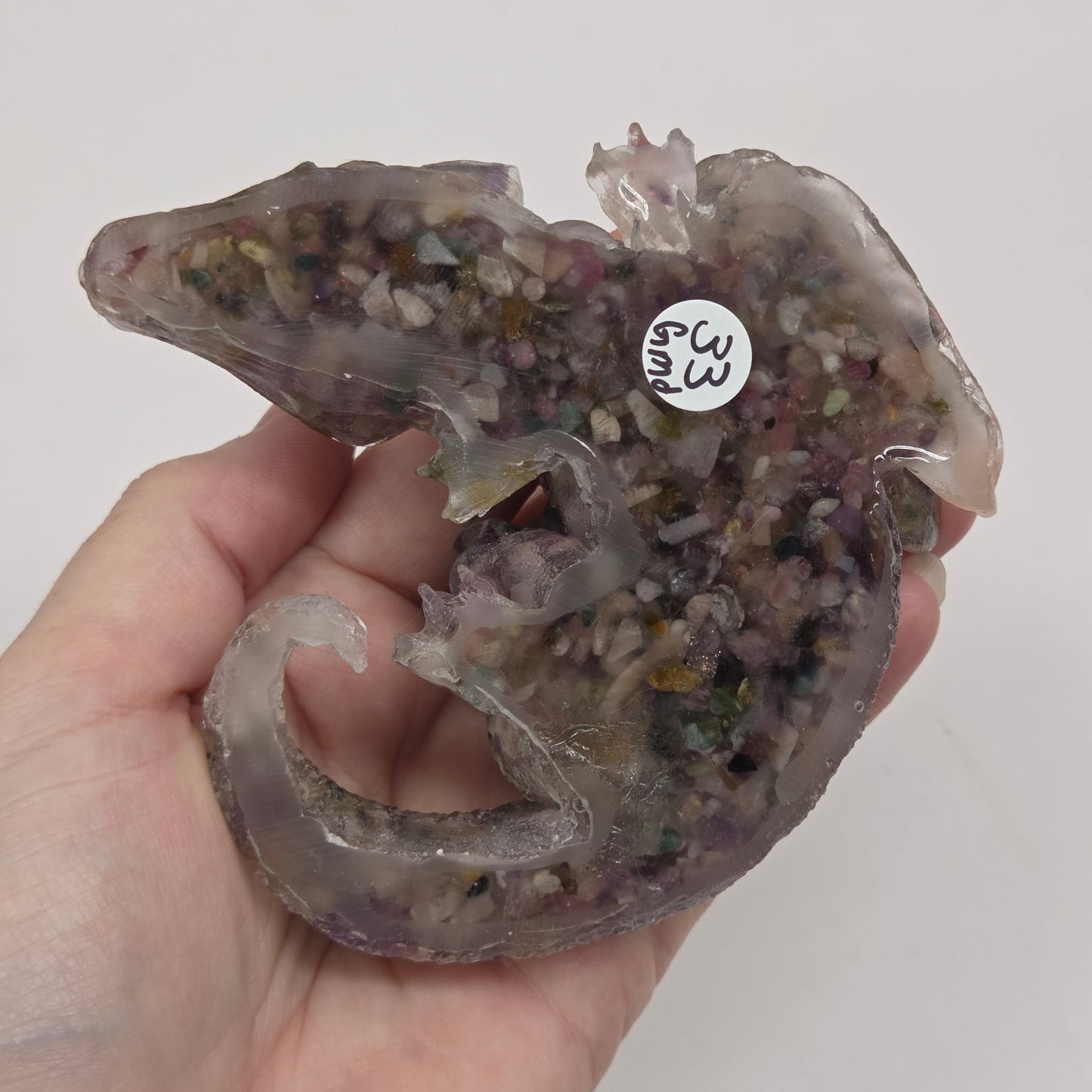 Hand holding resin with crystal chip carving of a dragon on a white background