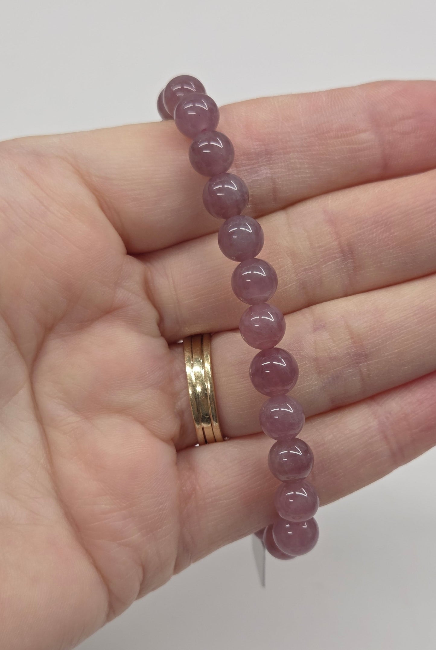 Hand wearing a pink beaded bracelet on a plain background