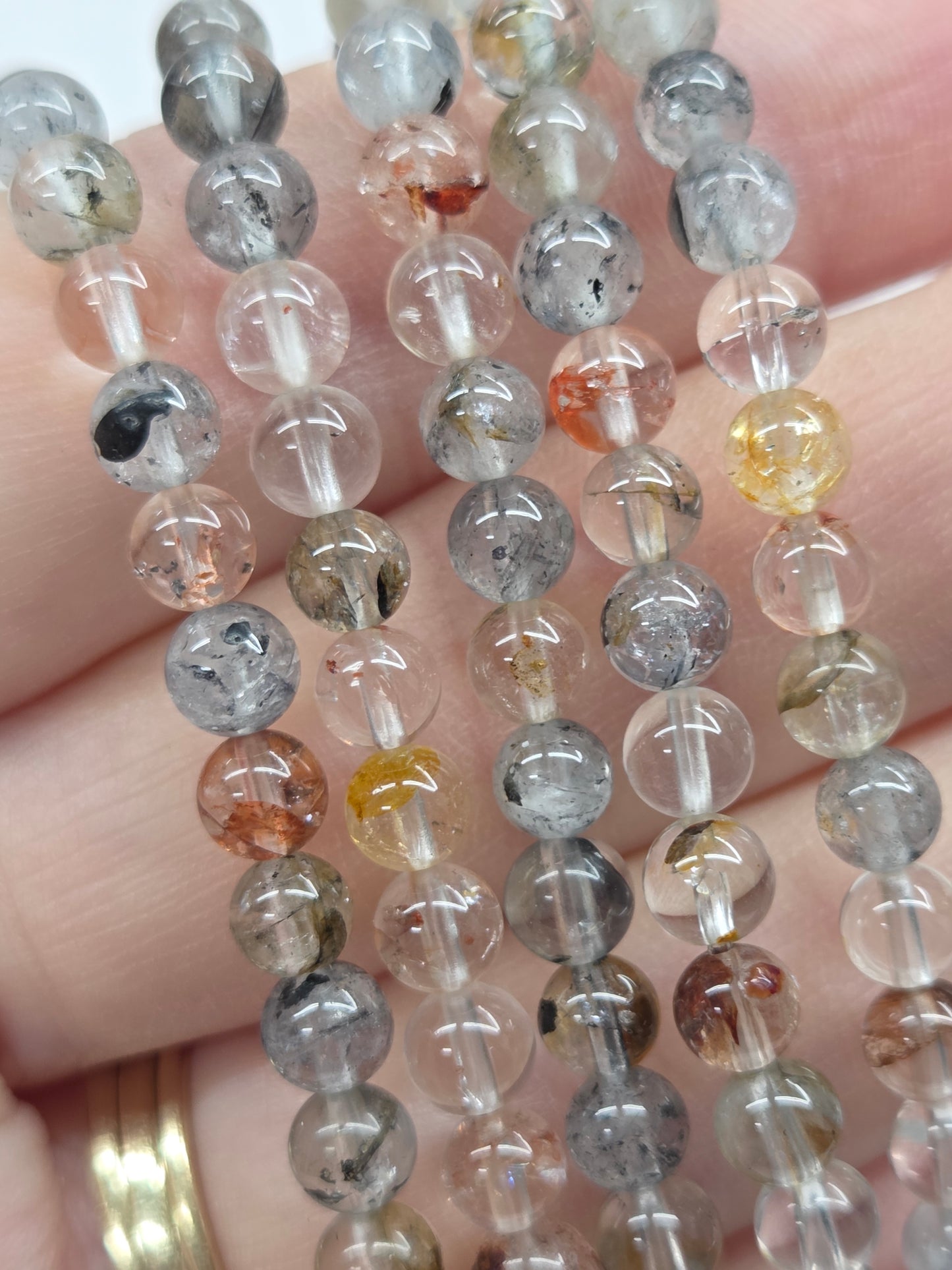 Close up of hand wearing multiple beaded bracelets on a plain background