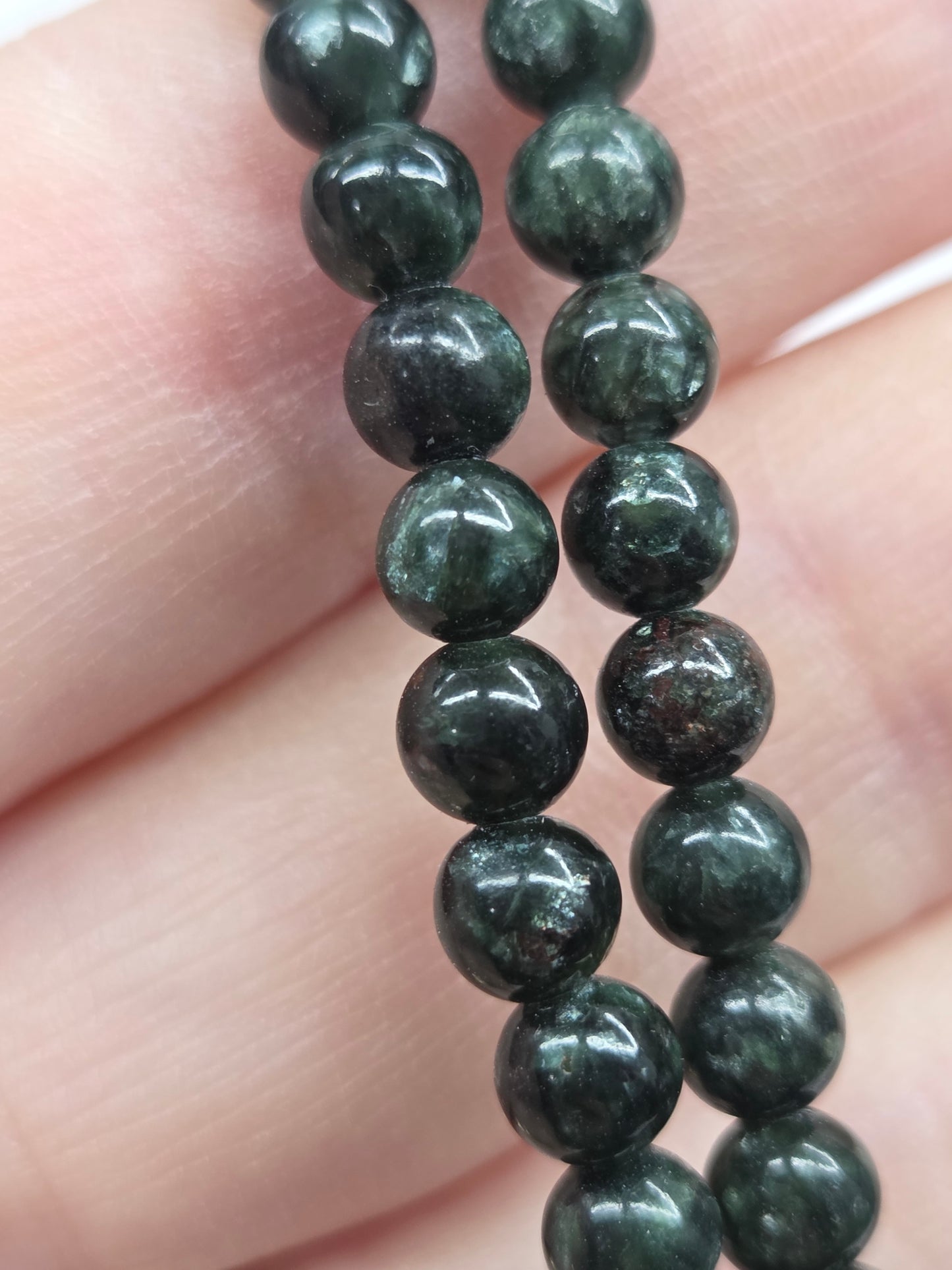 Close-up of a string of dark green beads on a person's hand.
