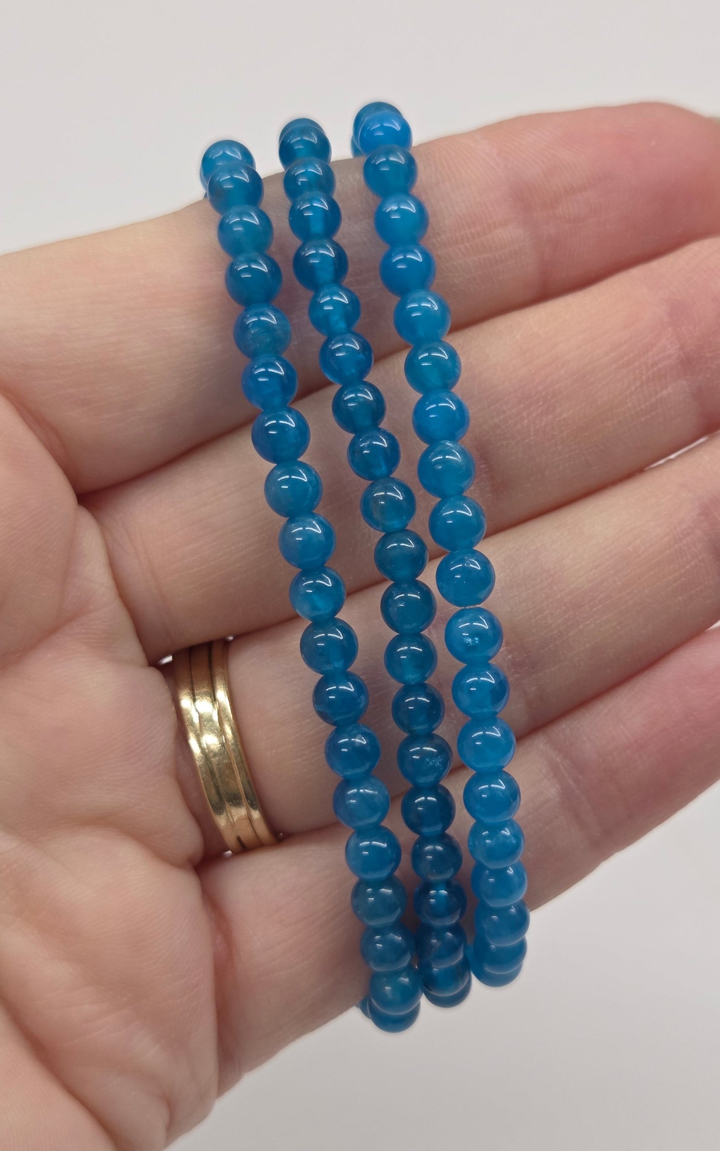 Hand wearing three blue beaded bracelets on a plain background